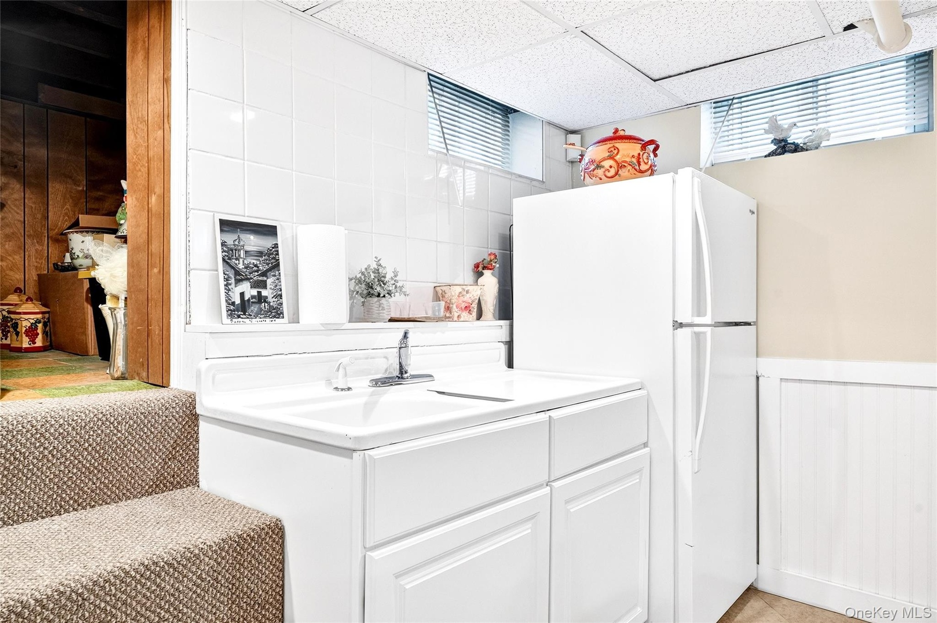 Kitchen with freestanding refrigerator, a wainscoted wall, a drop ceiling, white cabinets, and light countertops