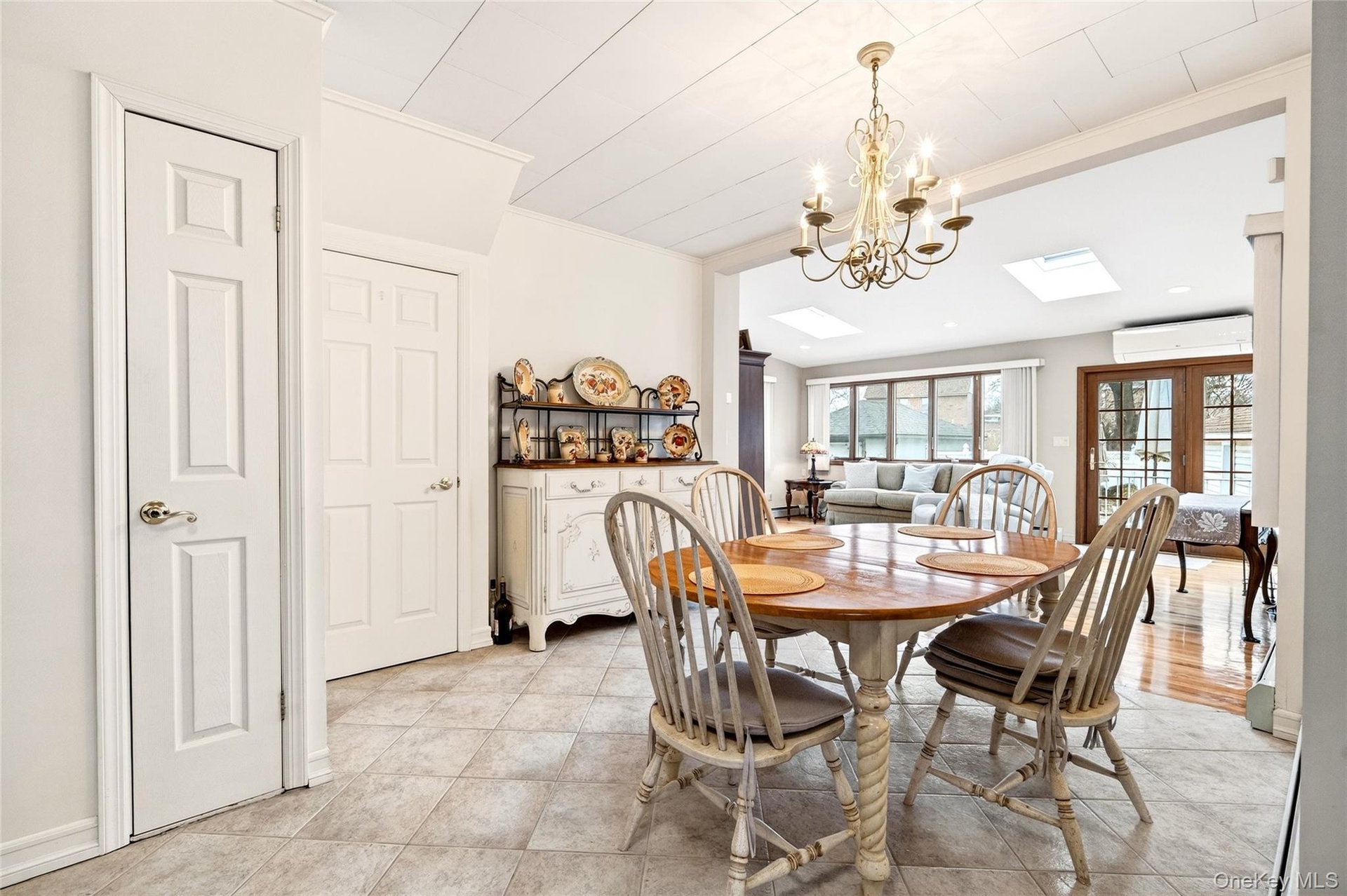 Dining room with crown molding, a chandelier, french doors, light tile patterned floors, and a skylight
