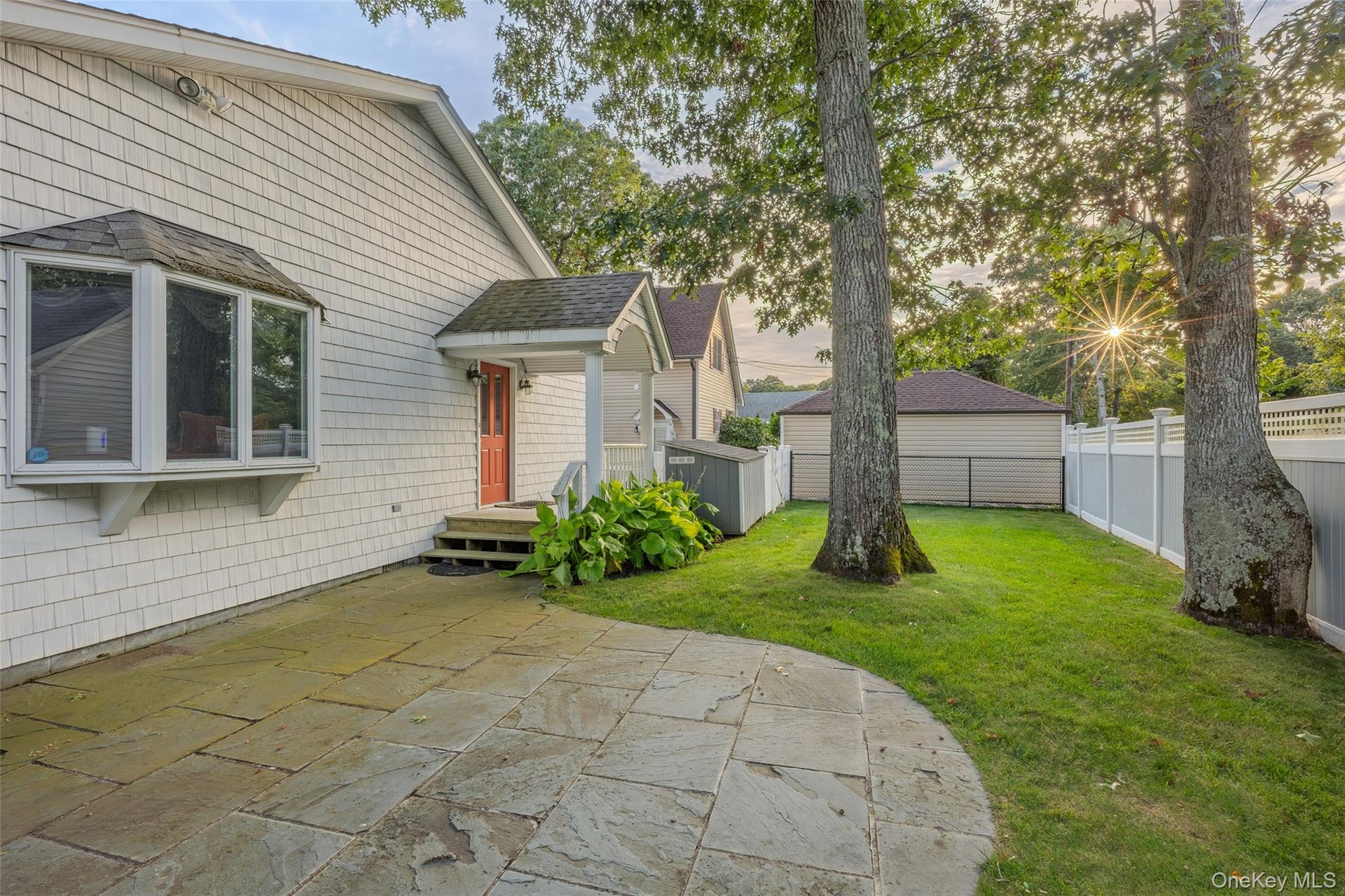 Stone patio with a curved edge, shingle siding, a bay window, and a covered entry