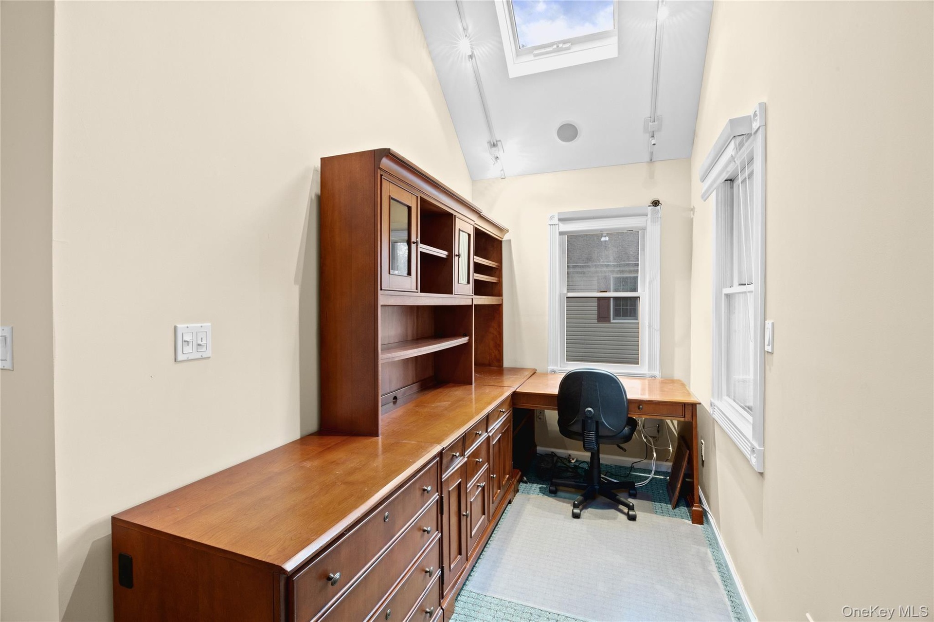 Built-in wood-finish desk with hutch and cabinetry, multiple windows, and a skylight