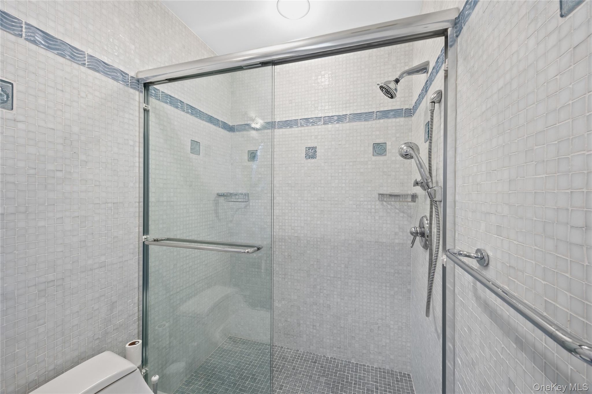 Glass-enclosed shower with a handheld shower fixture, overhead showerhead, and mosaic tile walls