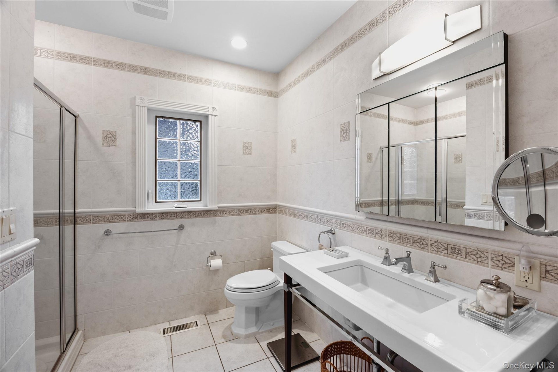 White ceramic tile flooring and wall accents, glass-enclosed shower, integrated sink vanity, multi-panel mirrored medicine cabinet, and a privacy wind