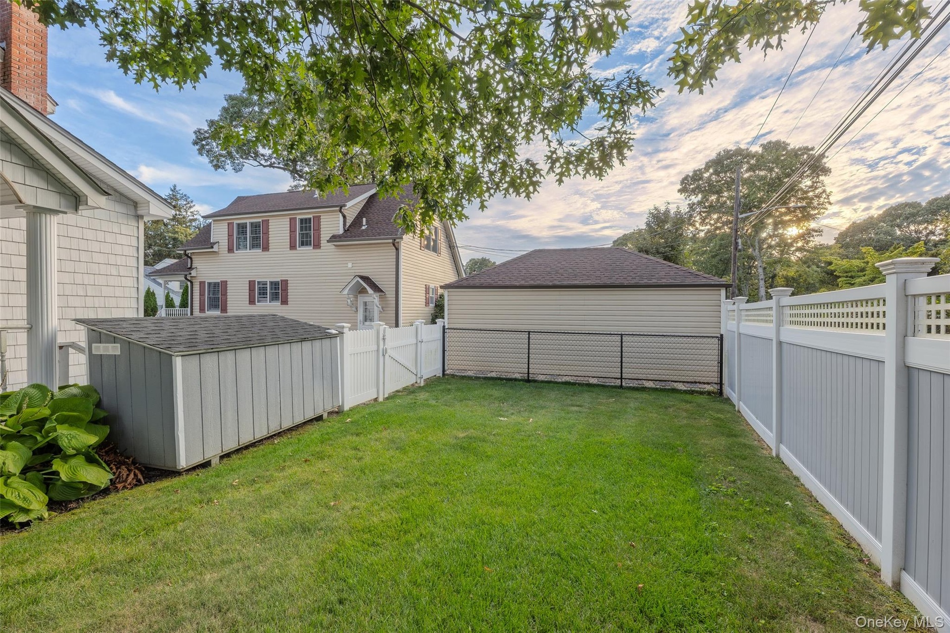Expansive lawn area, durable vinyl fencing, and a functional storage shed with sloped roof