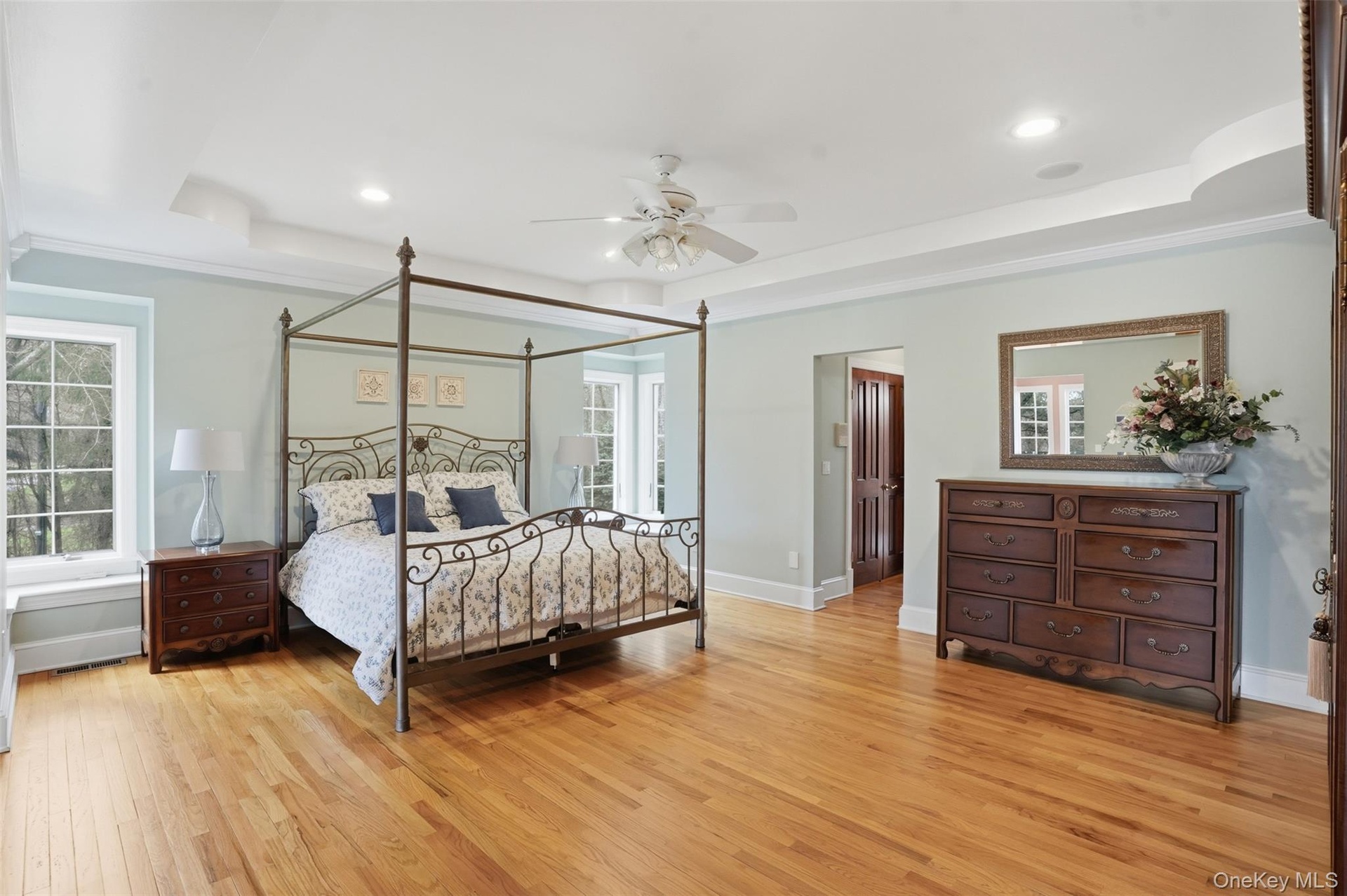 This expansive room features hardwood floors, light blue walls, and a white tray ceiling with recessed lighting