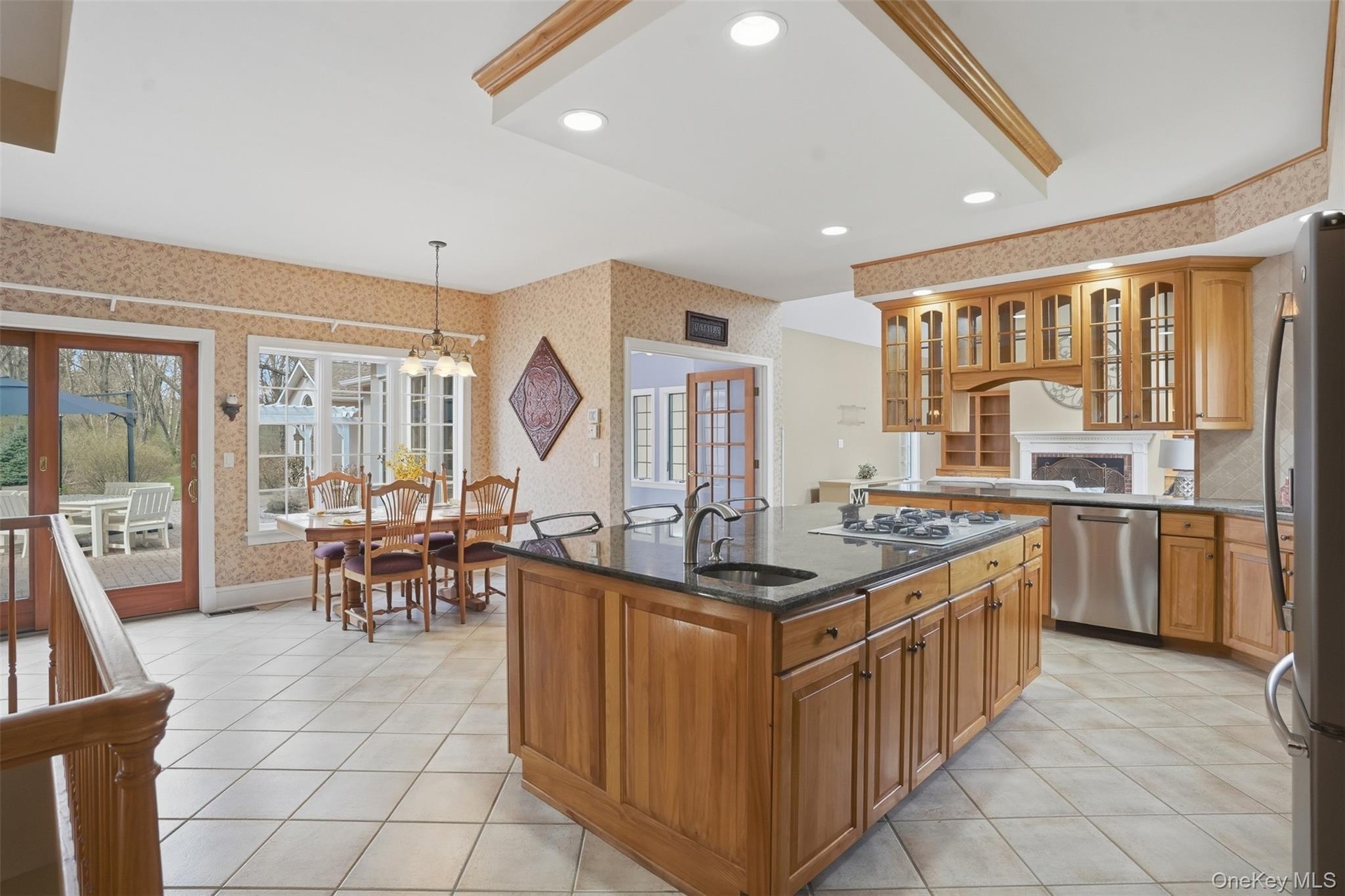 The kitchen features light wood cabinetry, a central island with a dark countertop and integrated sink, stainless steel appliances, and tiled flooring