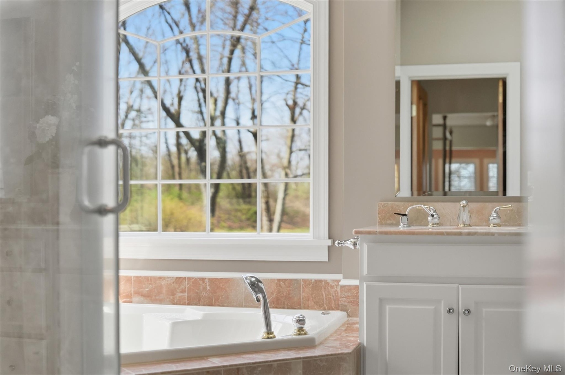 Bathroom featuring a built-in tub with a tiled surround, a large arched window, and a vanity with a light-colored countertop