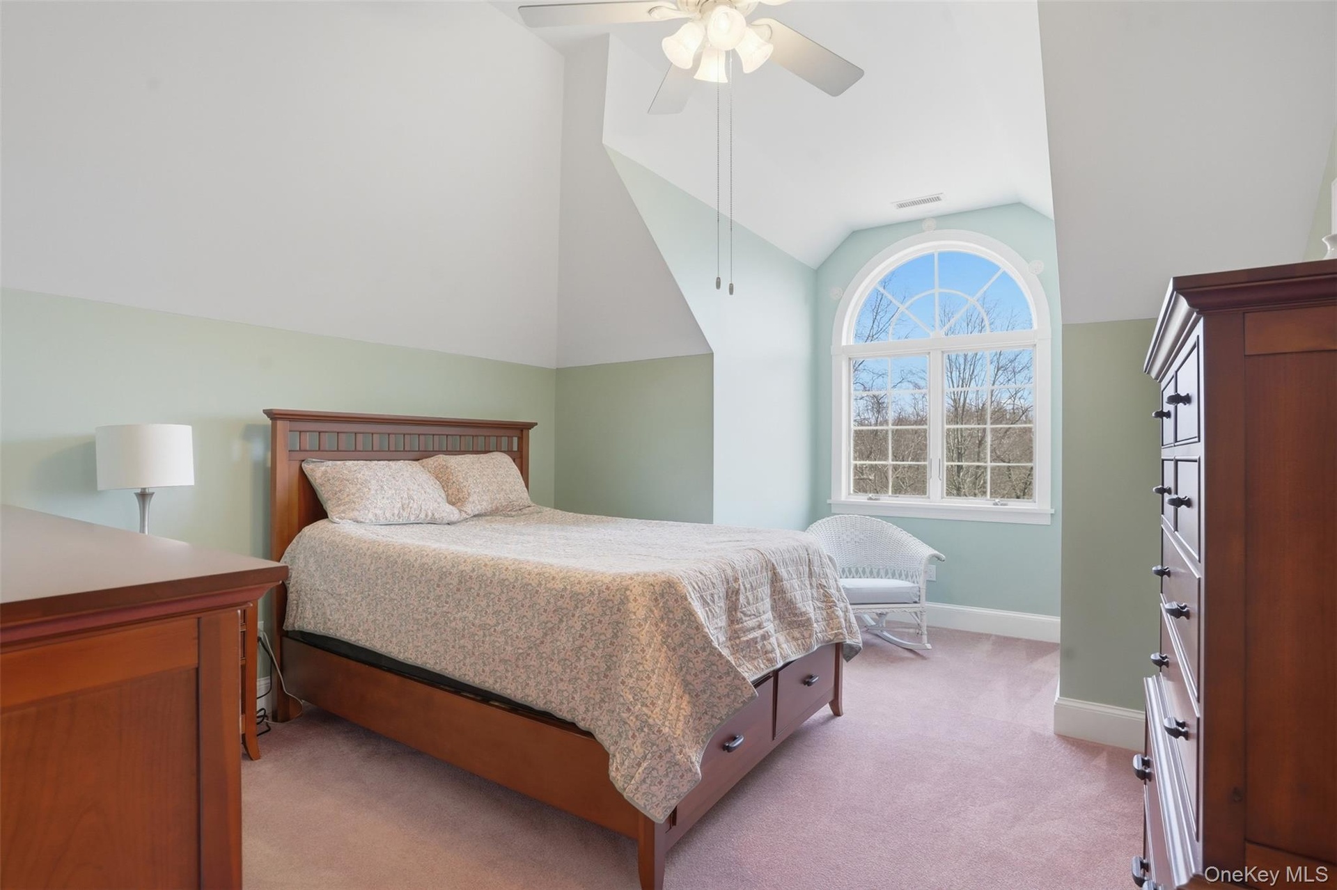 This room features an arched window with a wooded view, a sloped ceiling, and a ceiling fan