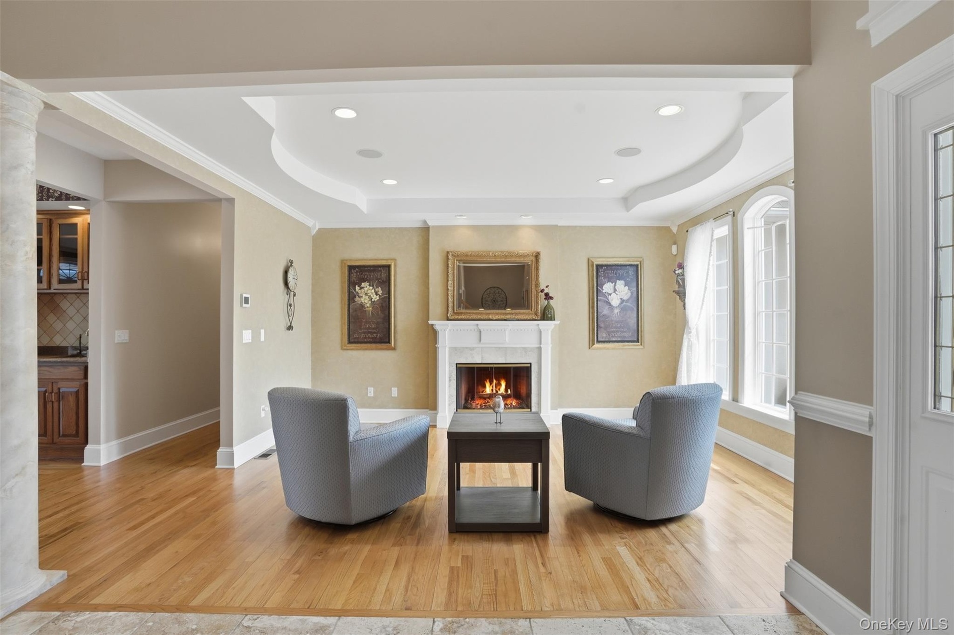 Living area featuring hardwood floors, a fireplace with a white mantel, recessed lighting, and large windows providing natural light