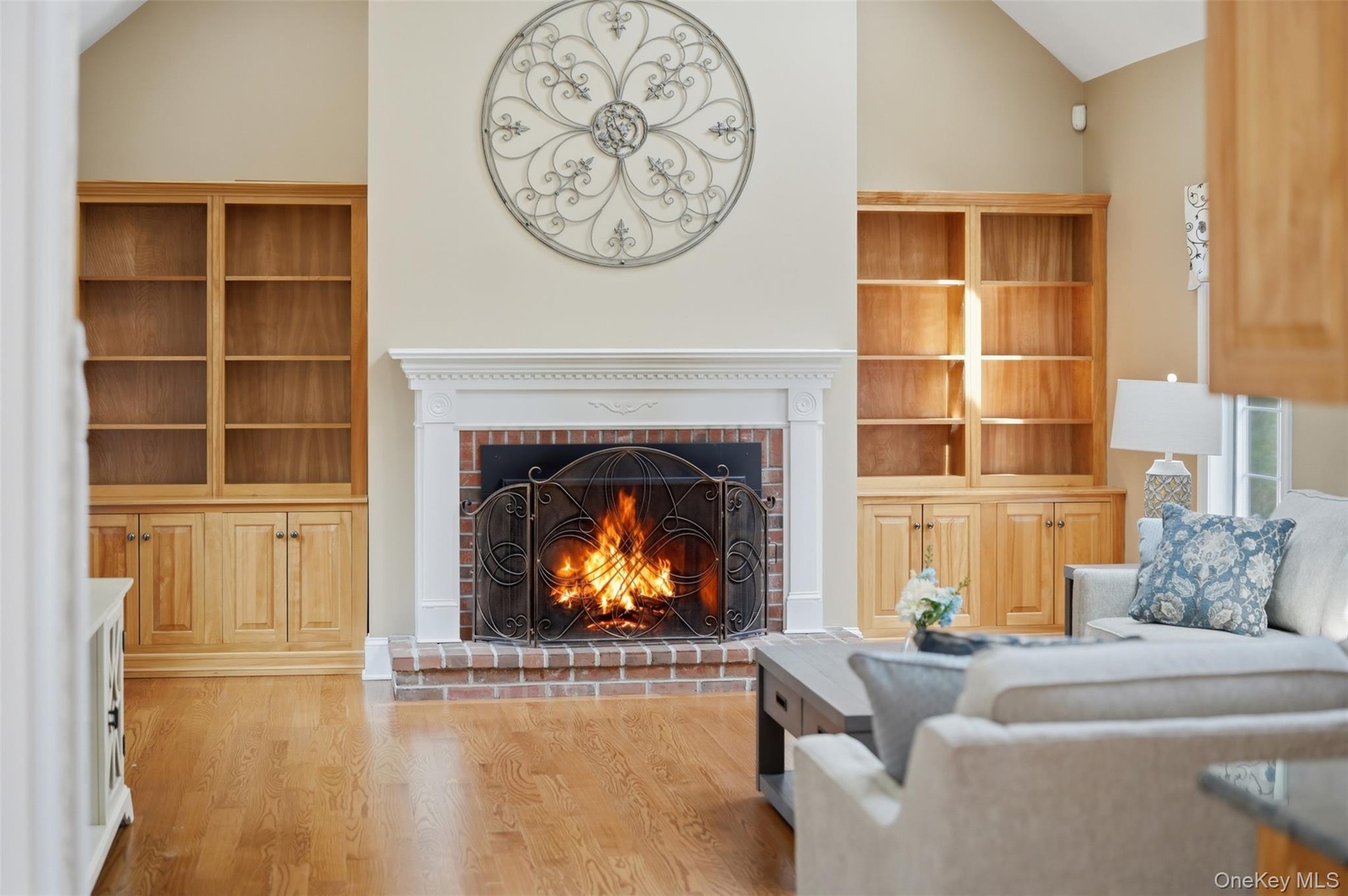 Living area featuring hardwood floors, a brick fireplace with a white mantel, and built-in wooden shelving units