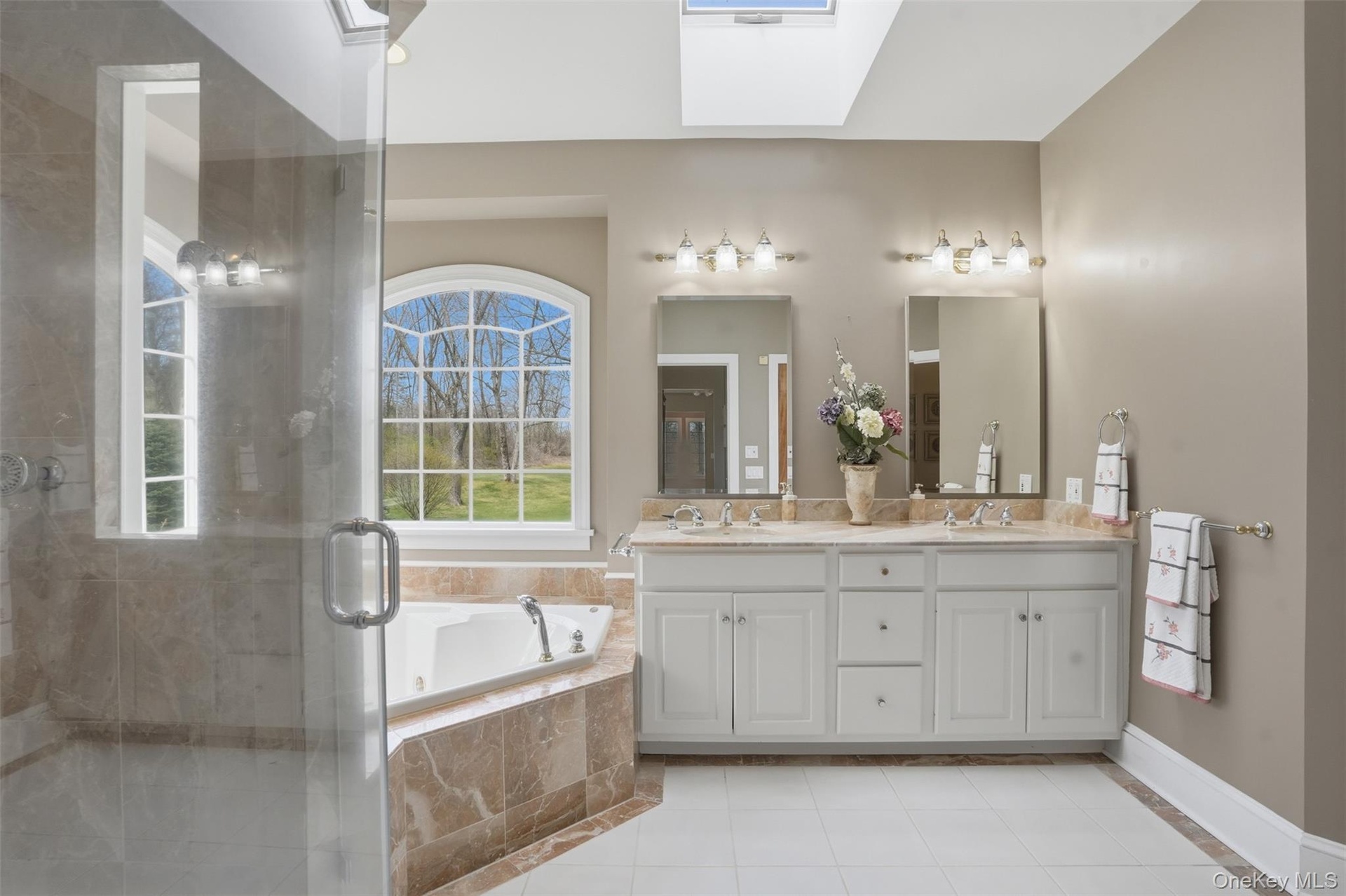 The bathroom features a spacious shower with a glass enclosure, a corner bathtub, and a dual vanity with two mirrors and overhead lighting