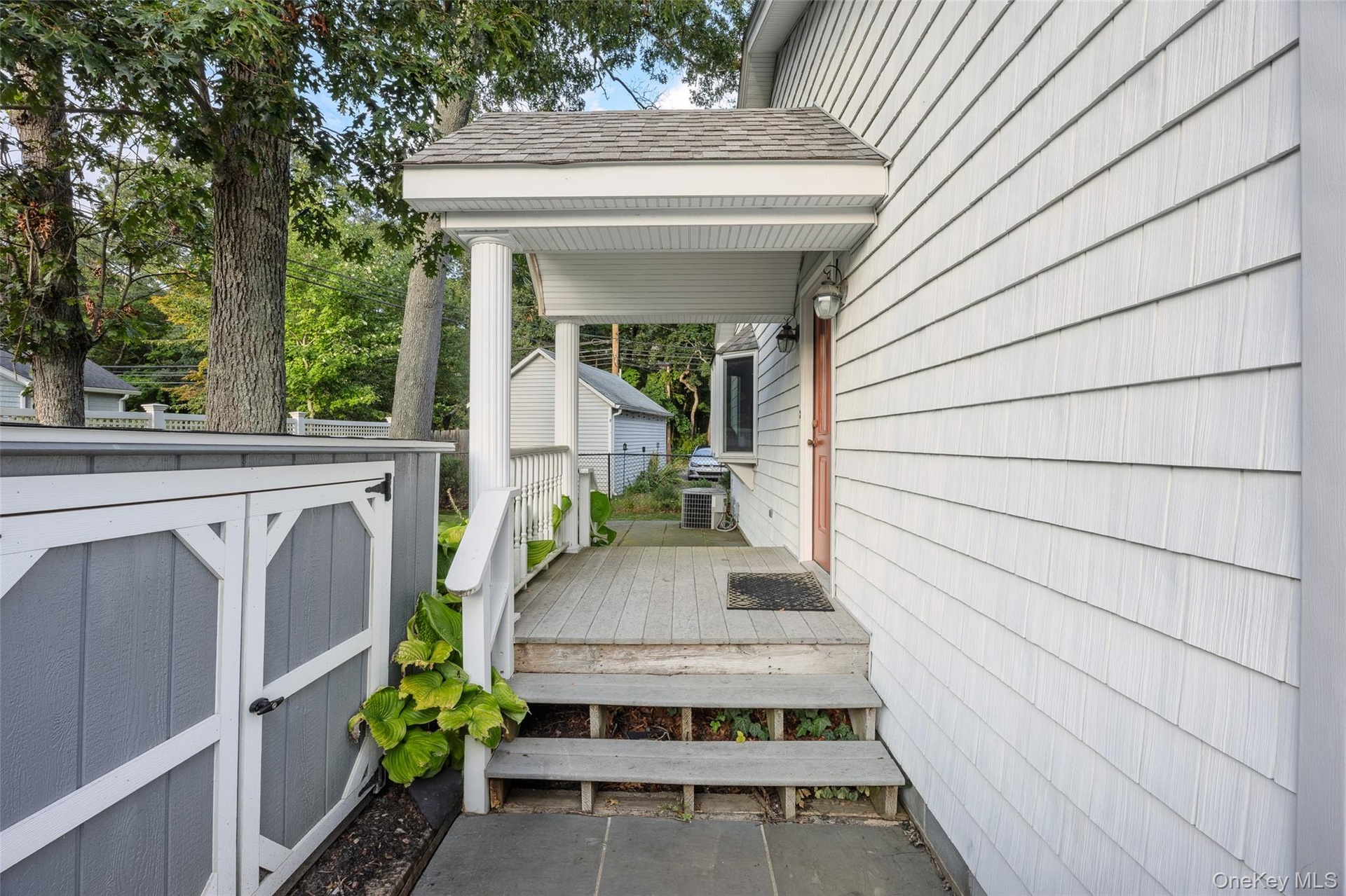 Covered porch with wood decking and white railing, leading to a paneled entry door