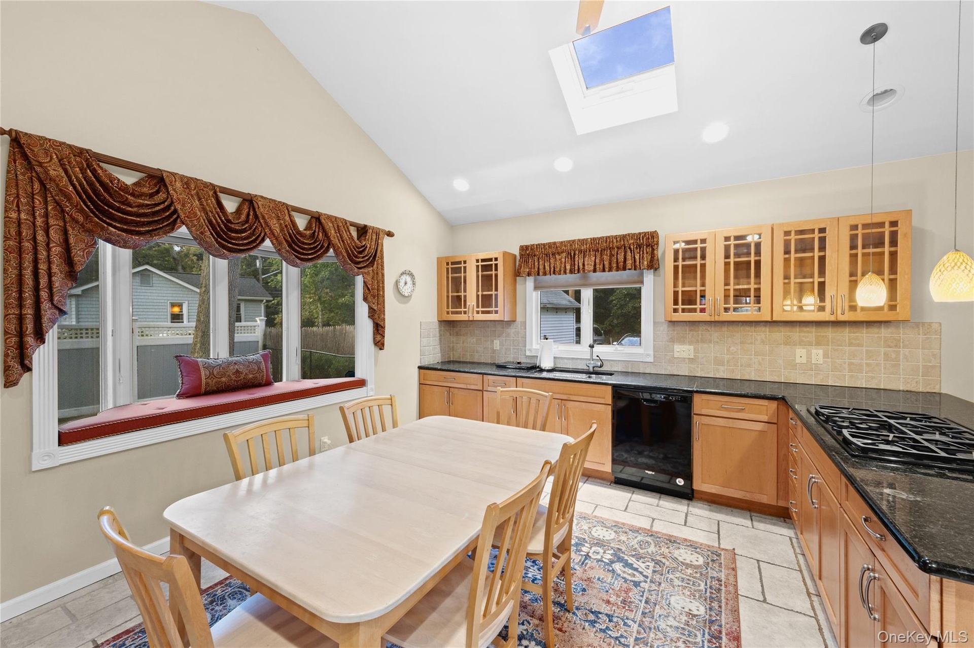 Kitchen featuring vaulted ceilings, a skylight, recessed lighting, wood cabinetry, and dark countertops