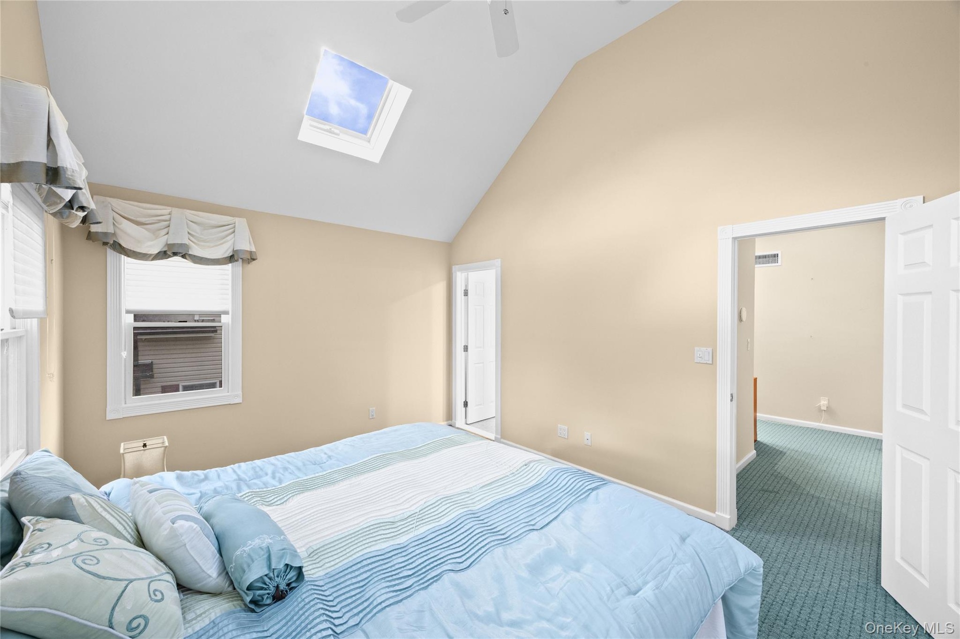 Vaulted ceiling, skylight, wall-mounted ceiling fan, window with blinds, and paneled interior doors