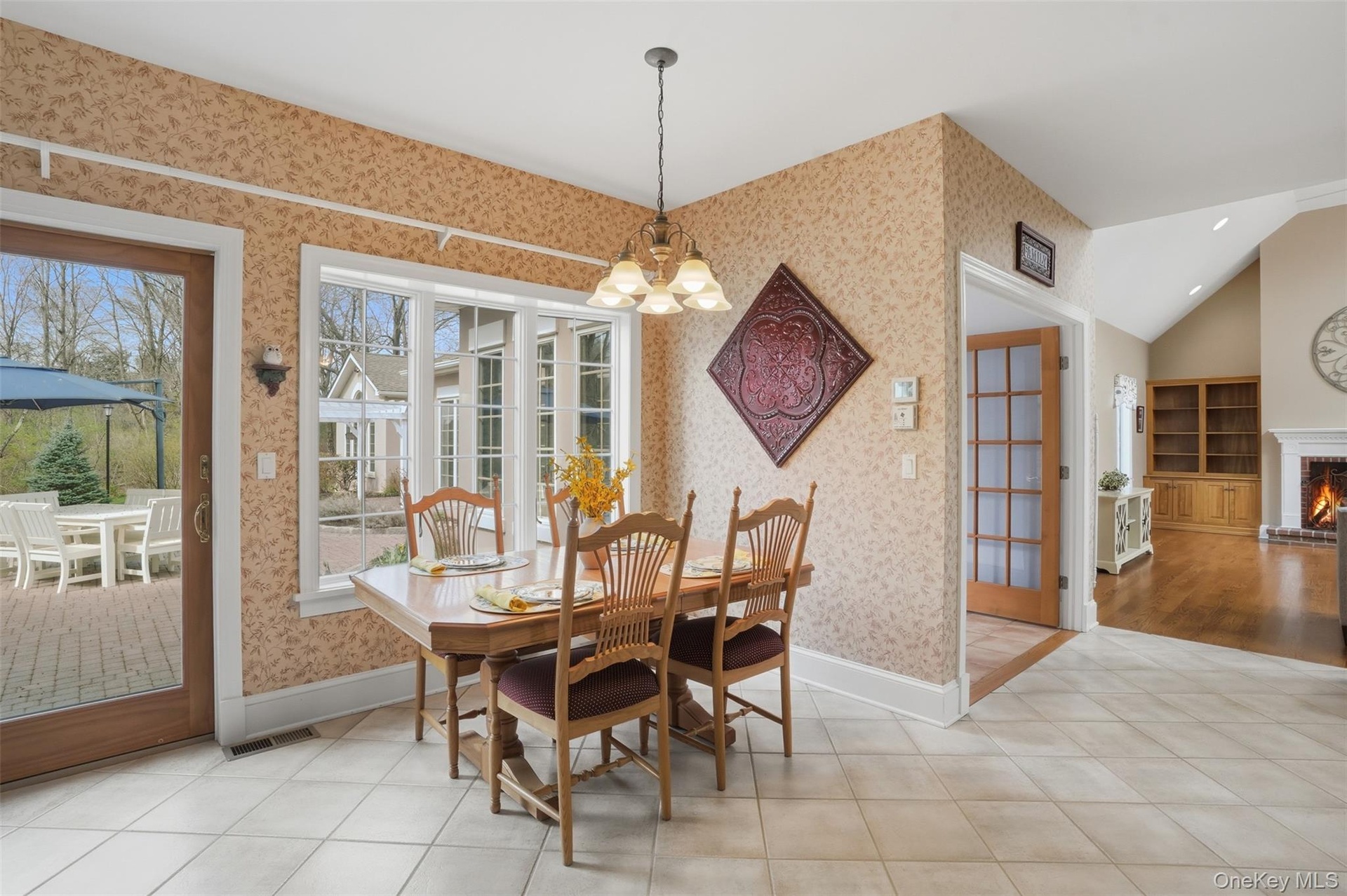 The dining area features tiled flooring, a decorative chandelier, and a window offering views of the exterior patio