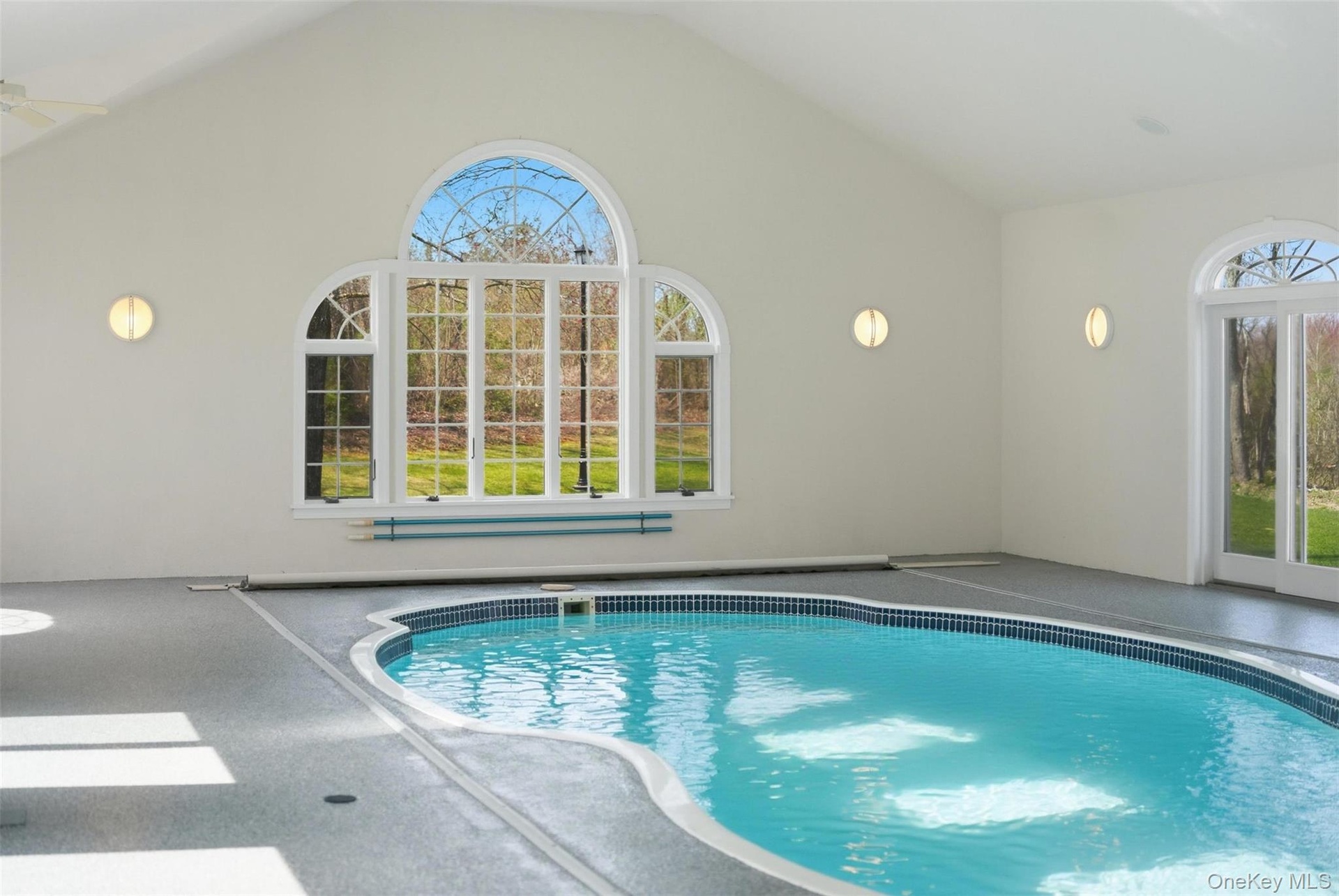 Indoor pool area featuring an arched window, a tiled pool with a blue interior, and access to the outdoors via French doors