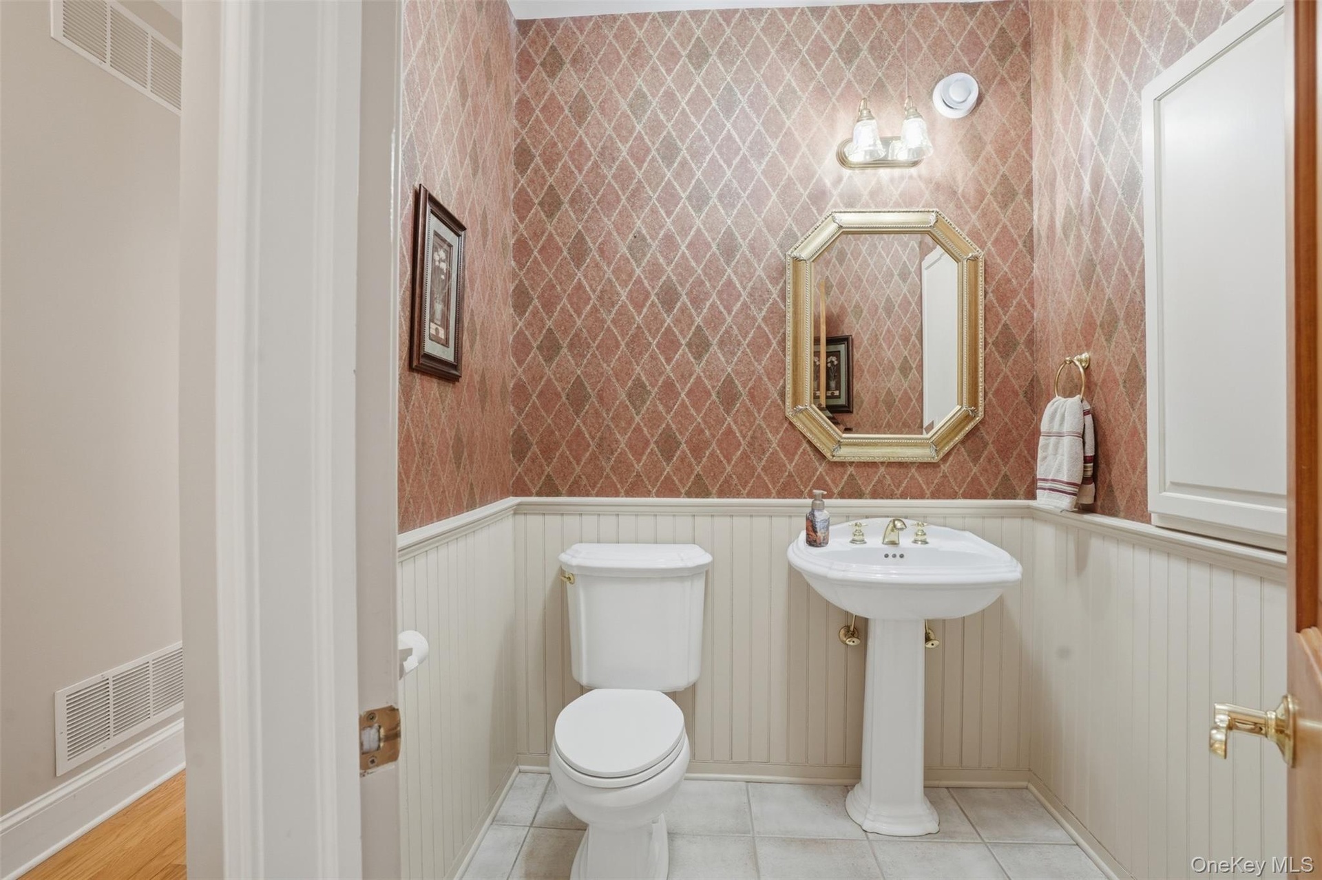 The powder room features a pedestal sink, white toilet, and patterned wallpaper above wainscoting