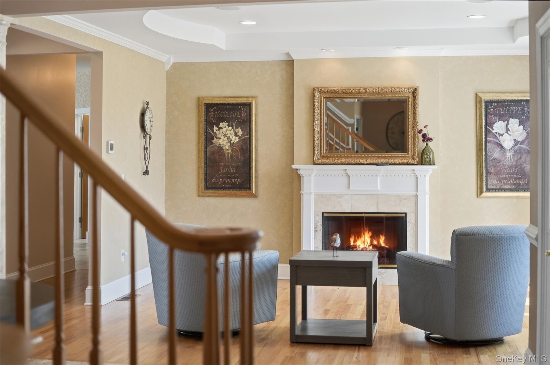 Living room featuring a fireplace with a stone surround and white mantle, warm-toned walls, and hardwood floors