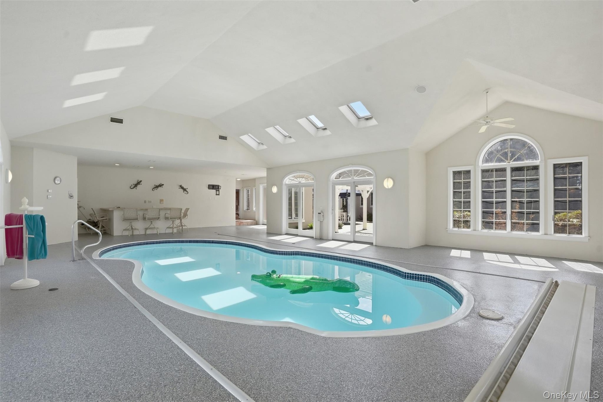 Indoor pool featuring skylights, large windows with arched transoms, and a wet bar area