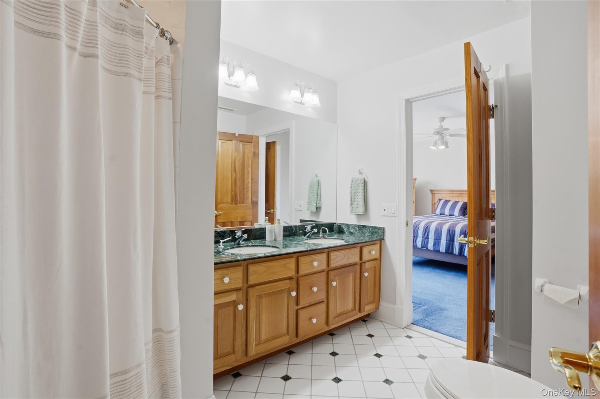 Bathroom featuring a double vanity with a green countertop, wood cabinetry, and a patterned tile floor