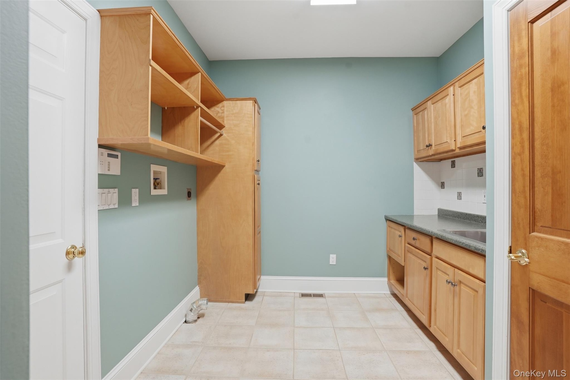 Utility room with light wood cabinetry, shelving, a countertop, and tiled flooring