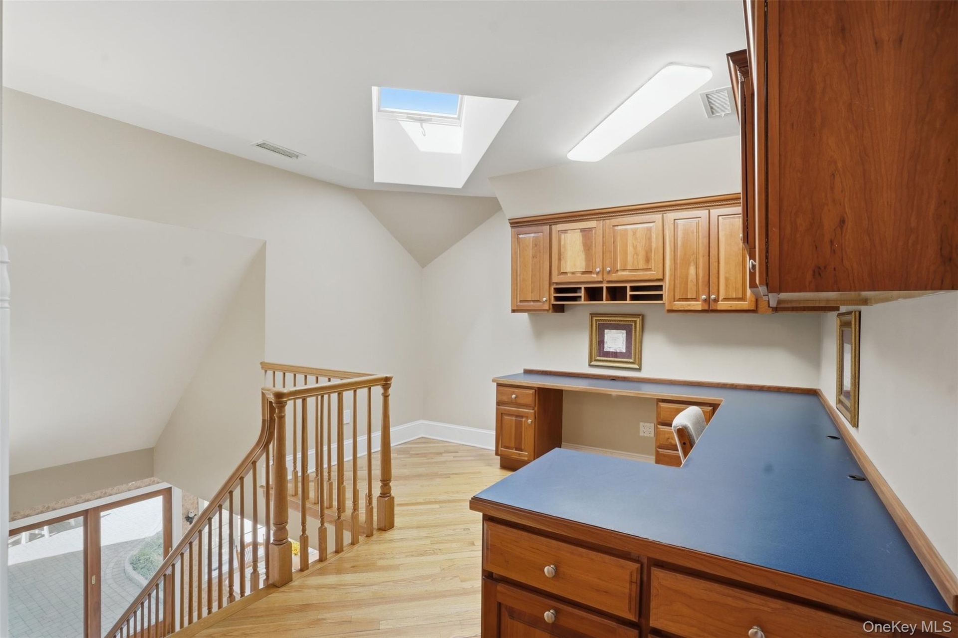 This versatile space features a built-in wooden desk and cabinetry, complemented by a skylight and hardwood flooring