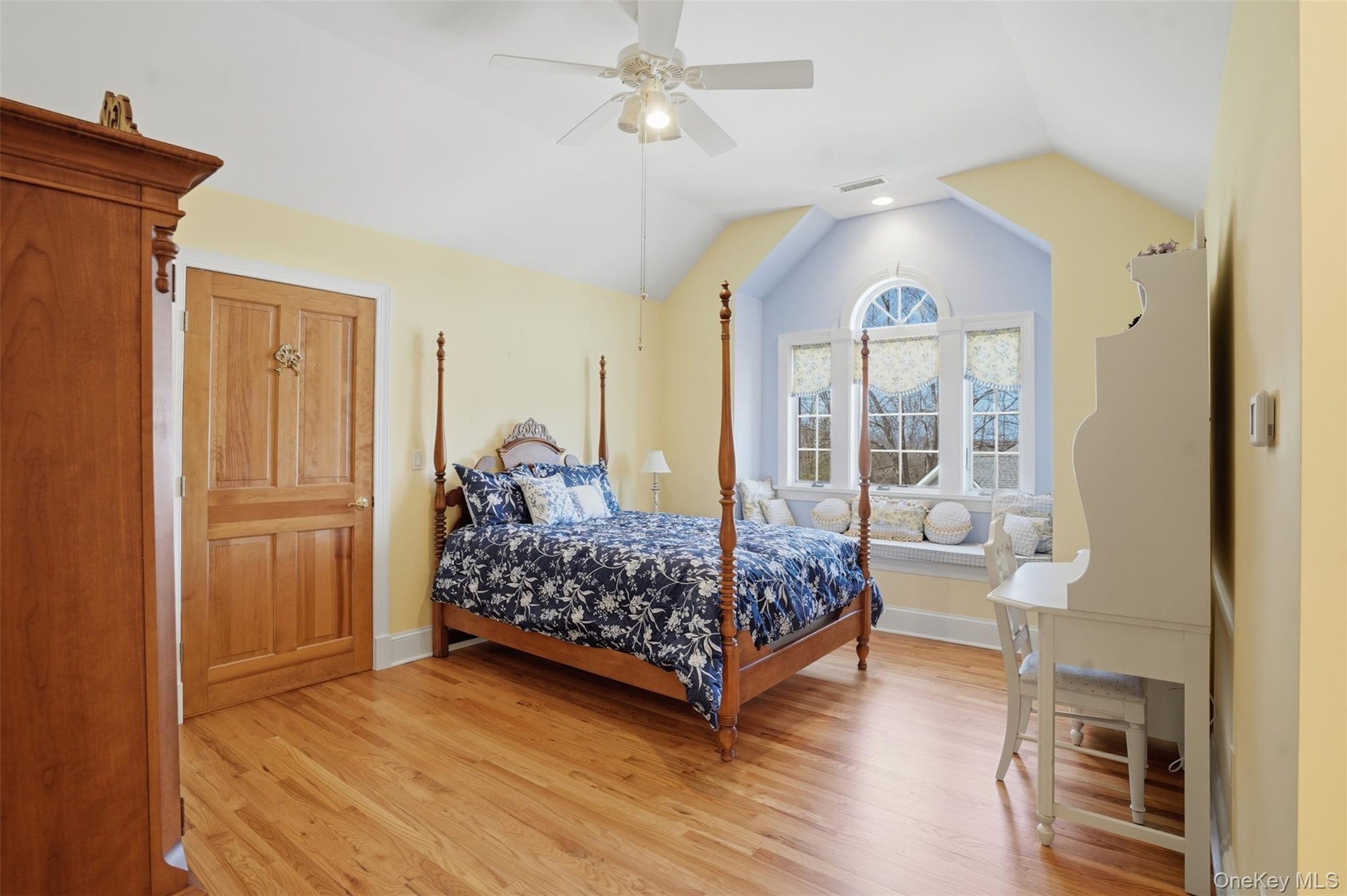 This room features light hardwood flooring, a window seat with a view, and a ceiling fan