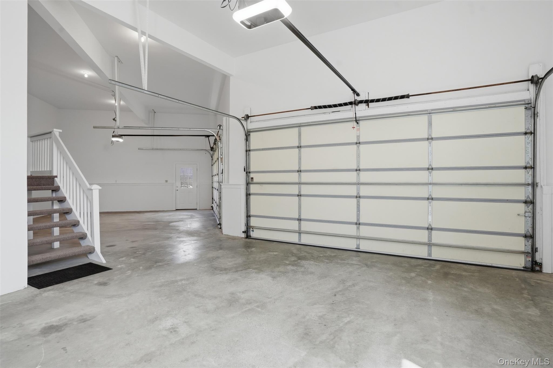 The property features an expansive garage with concrete flooring, a white automatic garage door, and a staircase with carpeted treads and white railin