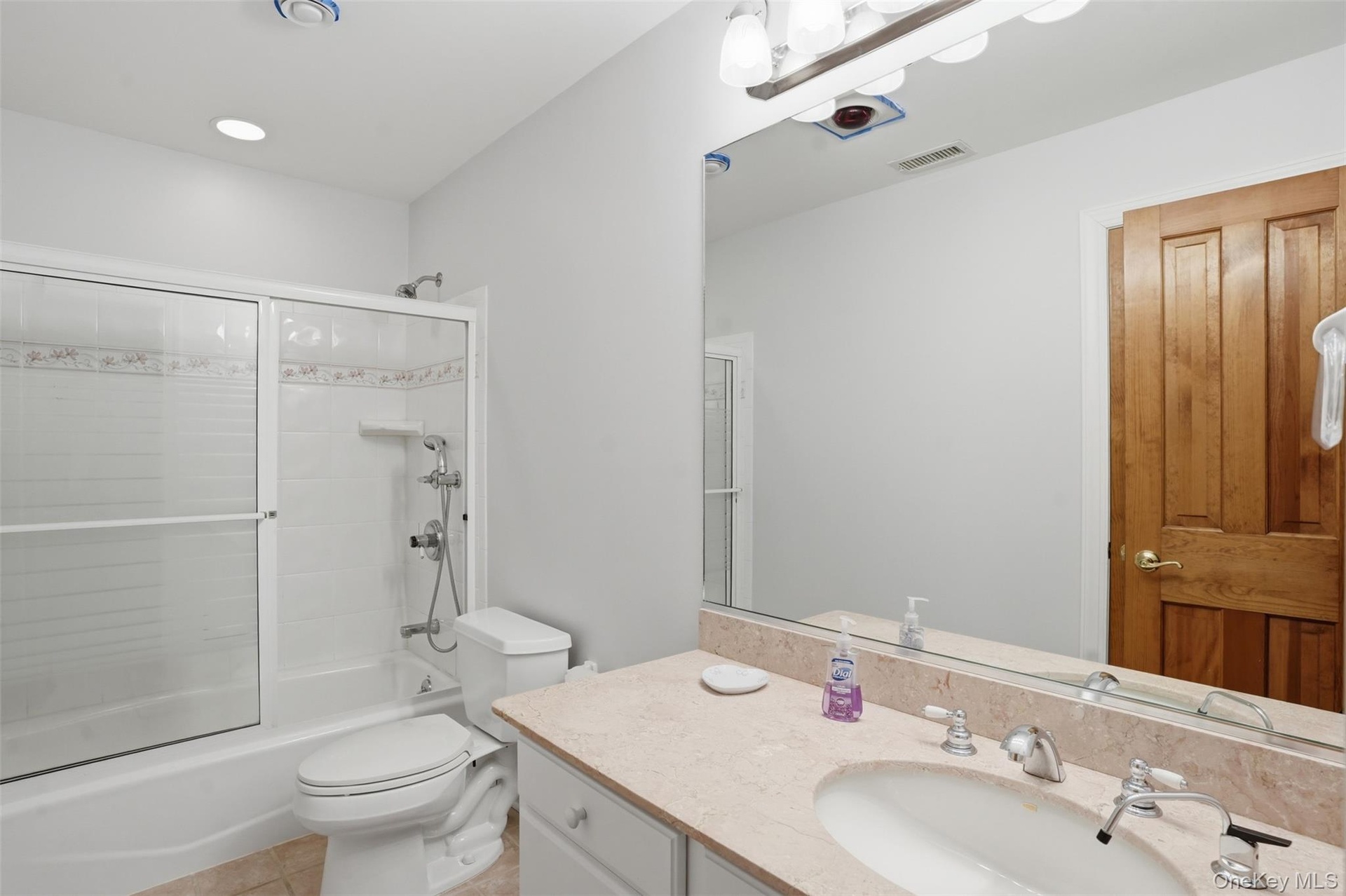 The bathroom features a vanity with a light-colored countertop and a mirror, and a shower-tub combination with sliding glass doors