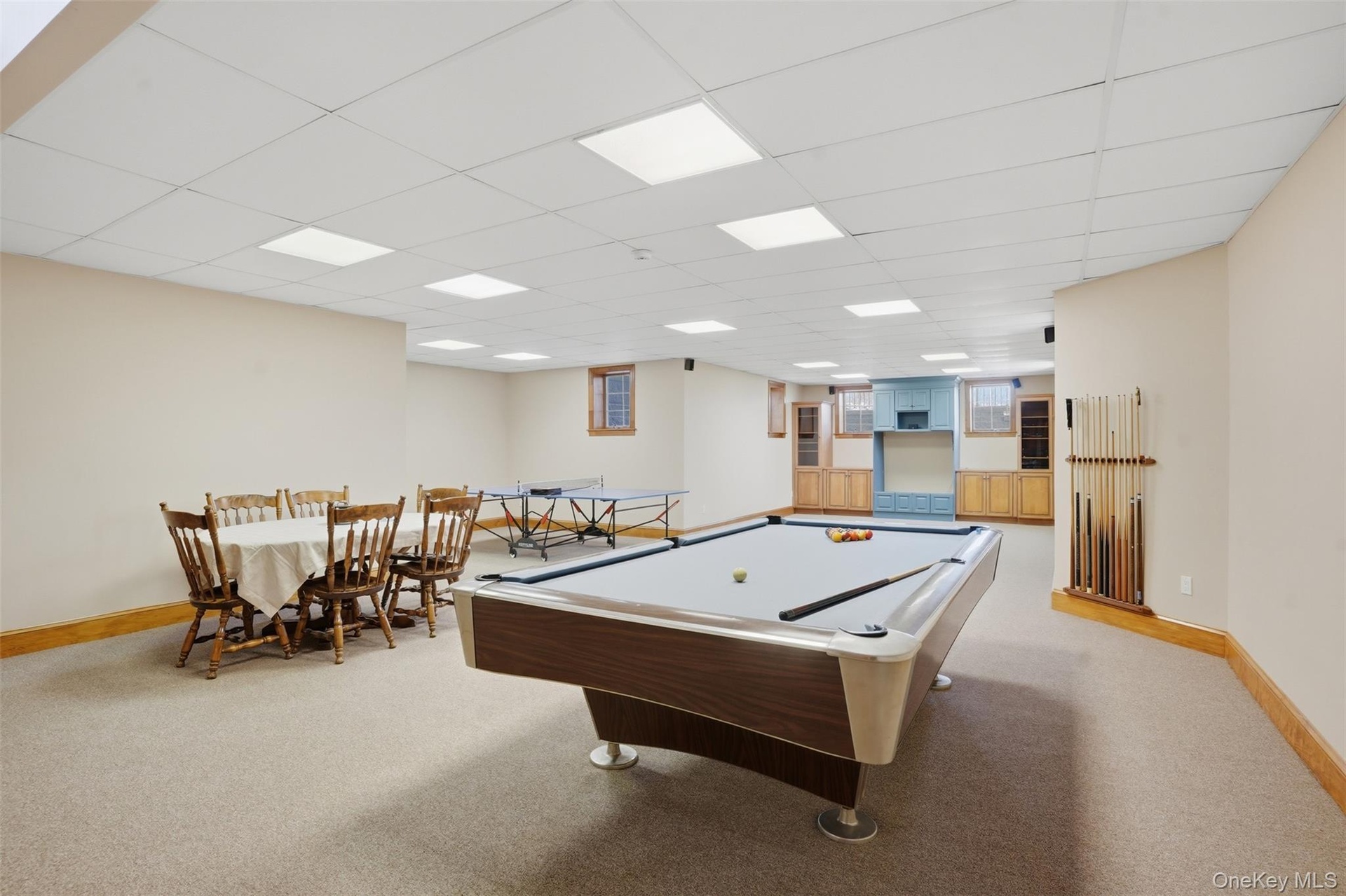 Spacious recreation room featuring carpeted flooring, recessed lighting, and a built-in entertainment area with light blue and natural wood cabinetry