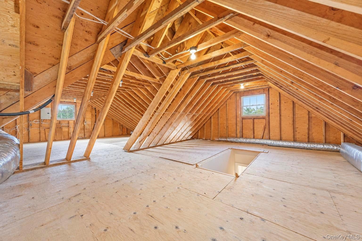 Open attic space with exposed wood rafters, plywood subflooring, and two operable windows