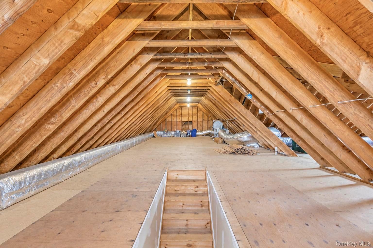Steps to full attic ,Exposed wood rafters, plywood flooring, and ceiling-mounted lighting fixtures