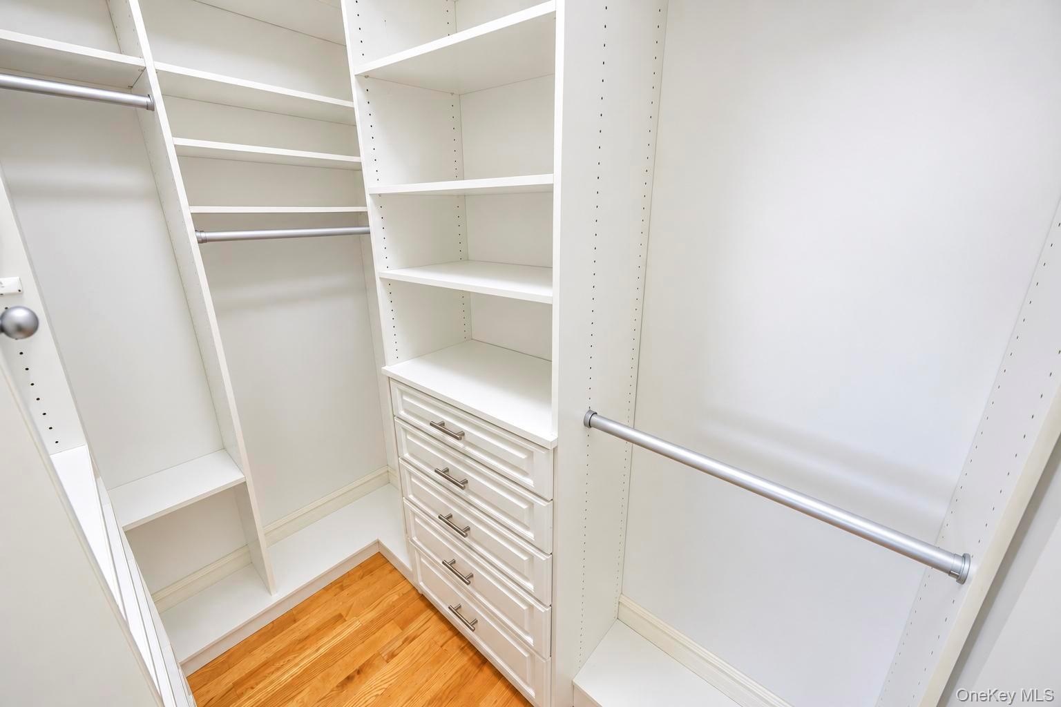 Custom closet system featuring white shelving, multiple hanging rods, and built-in drawers with brushed nickel hardware