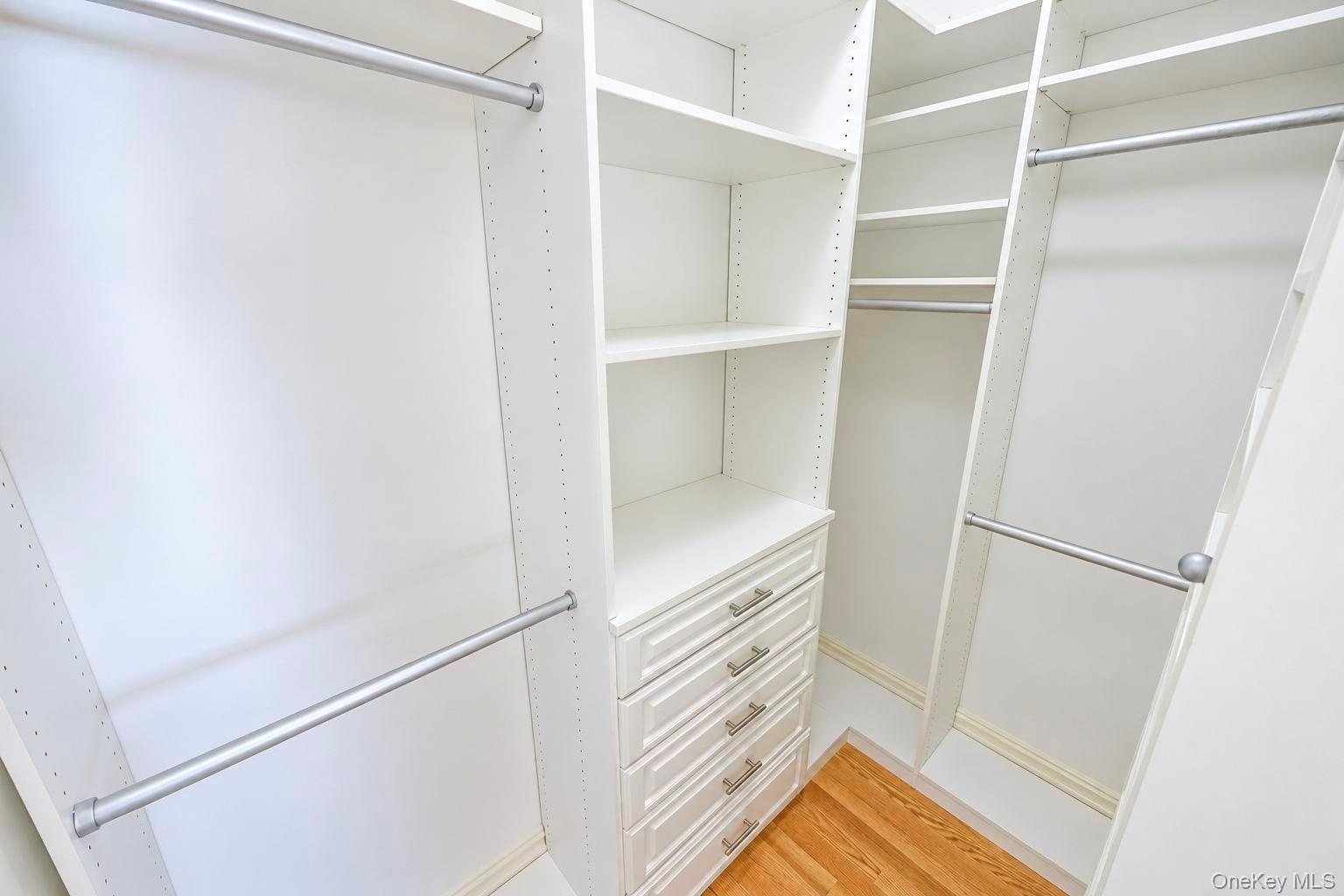 Custom closet system featuring multiple hanging rods, built-in shelving, integrated drawers with brushed nickel hardware, and wood-finish flooring