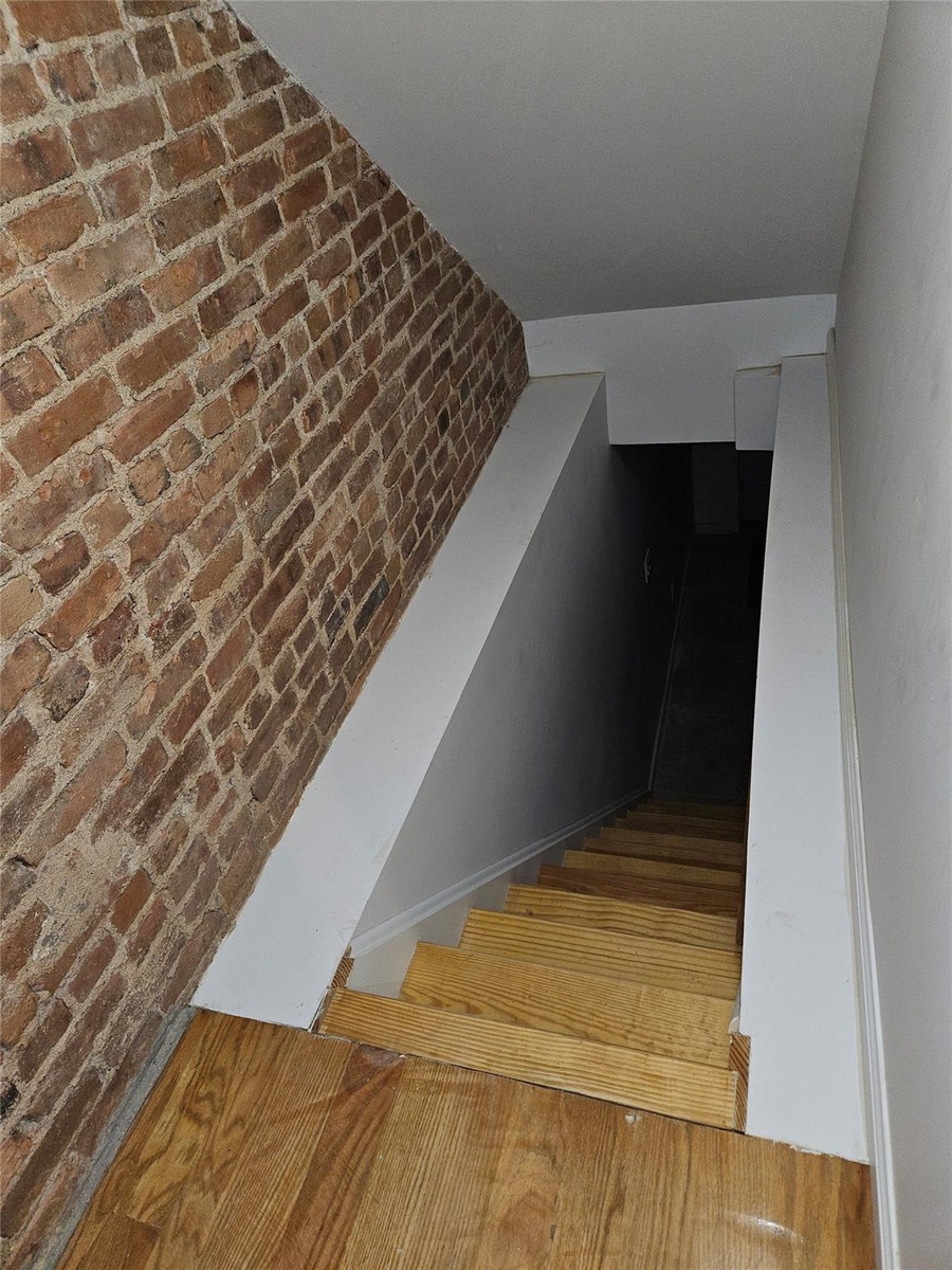 Staircase with wood finished floors and brick wall