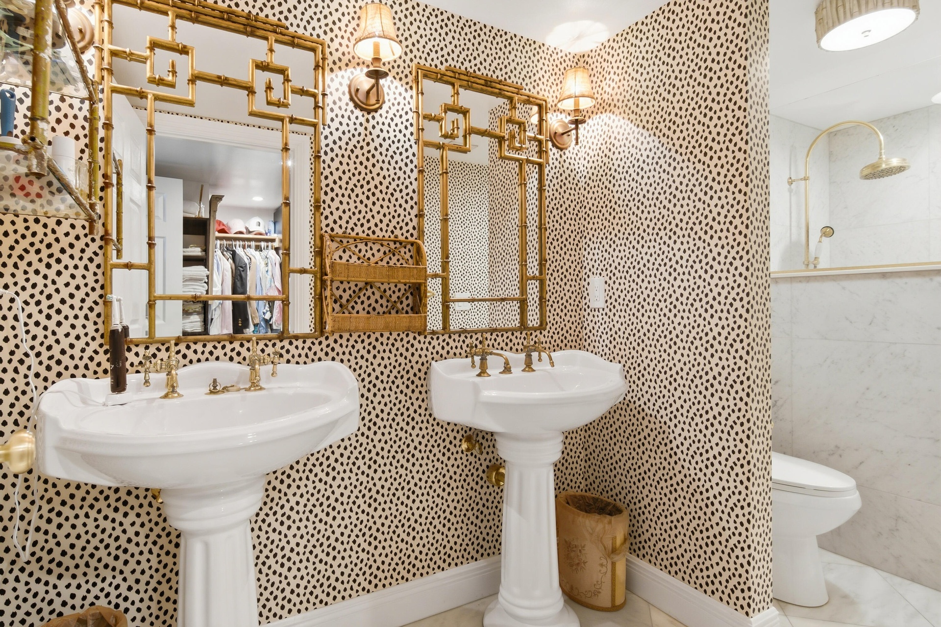 Dual pedestal sinks with brass fixtures, gold-framed decorative mirrors, and wall-mounted sconces