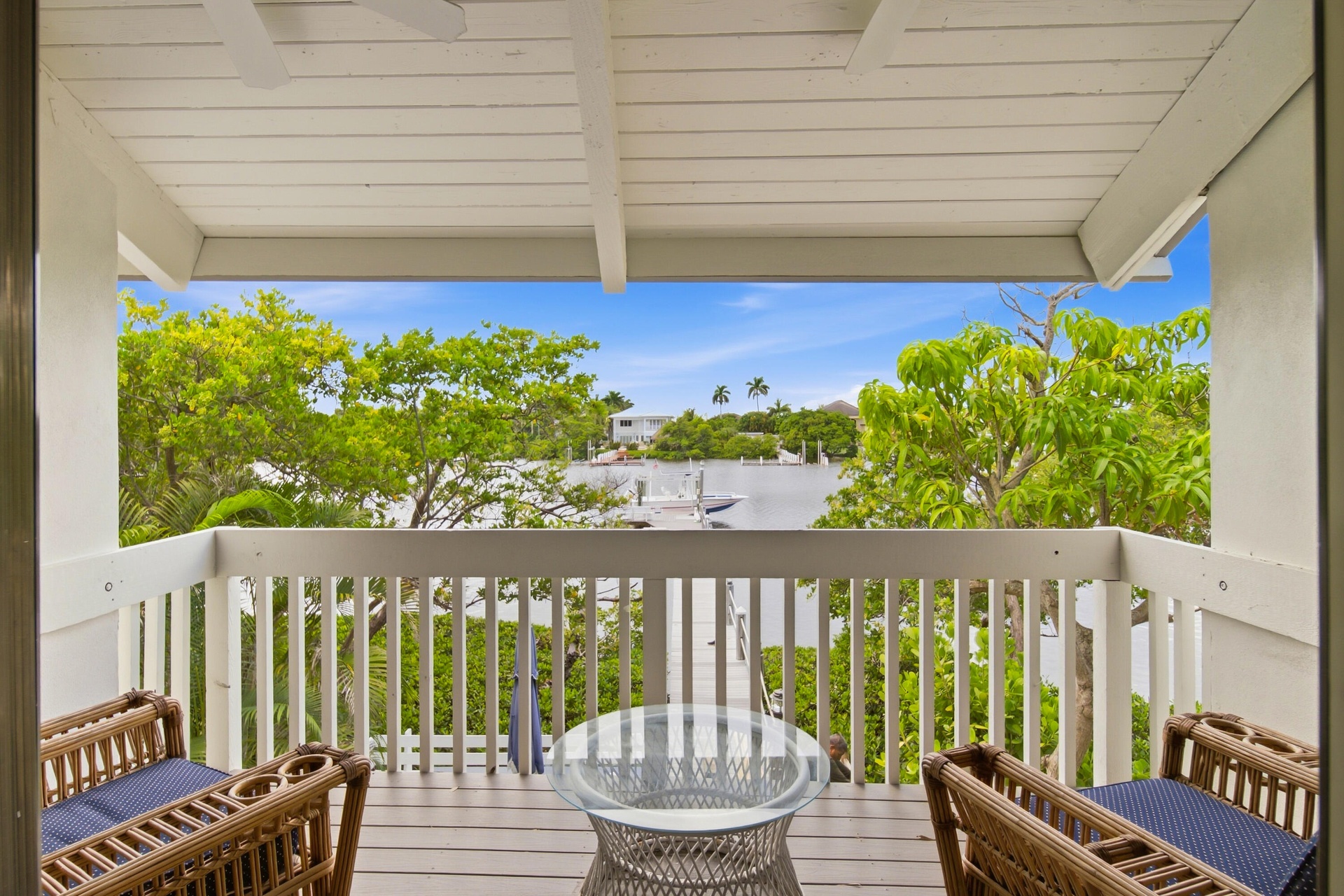 Covered balcony with white wood-plank flooring, white railing, and water frontage