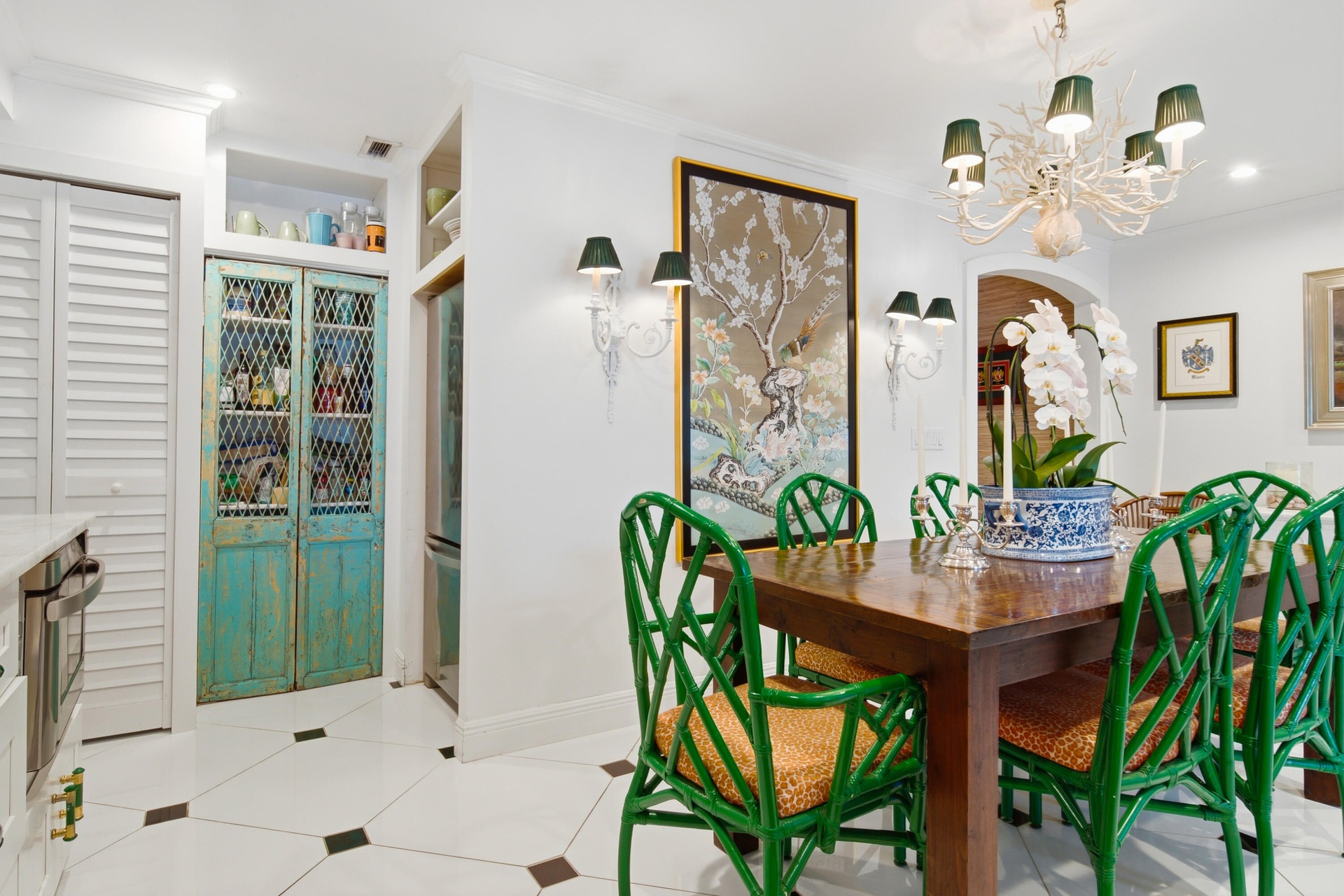 White tile flooring with black diamond inlays, built-in storage with distressed teal doors, and a decorative chandelier with green shades