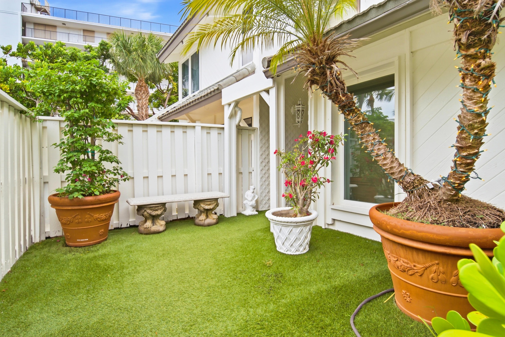 Private outdoor space featuring artificial turf, a white privacy fence, a decorative stone bench, and a large window