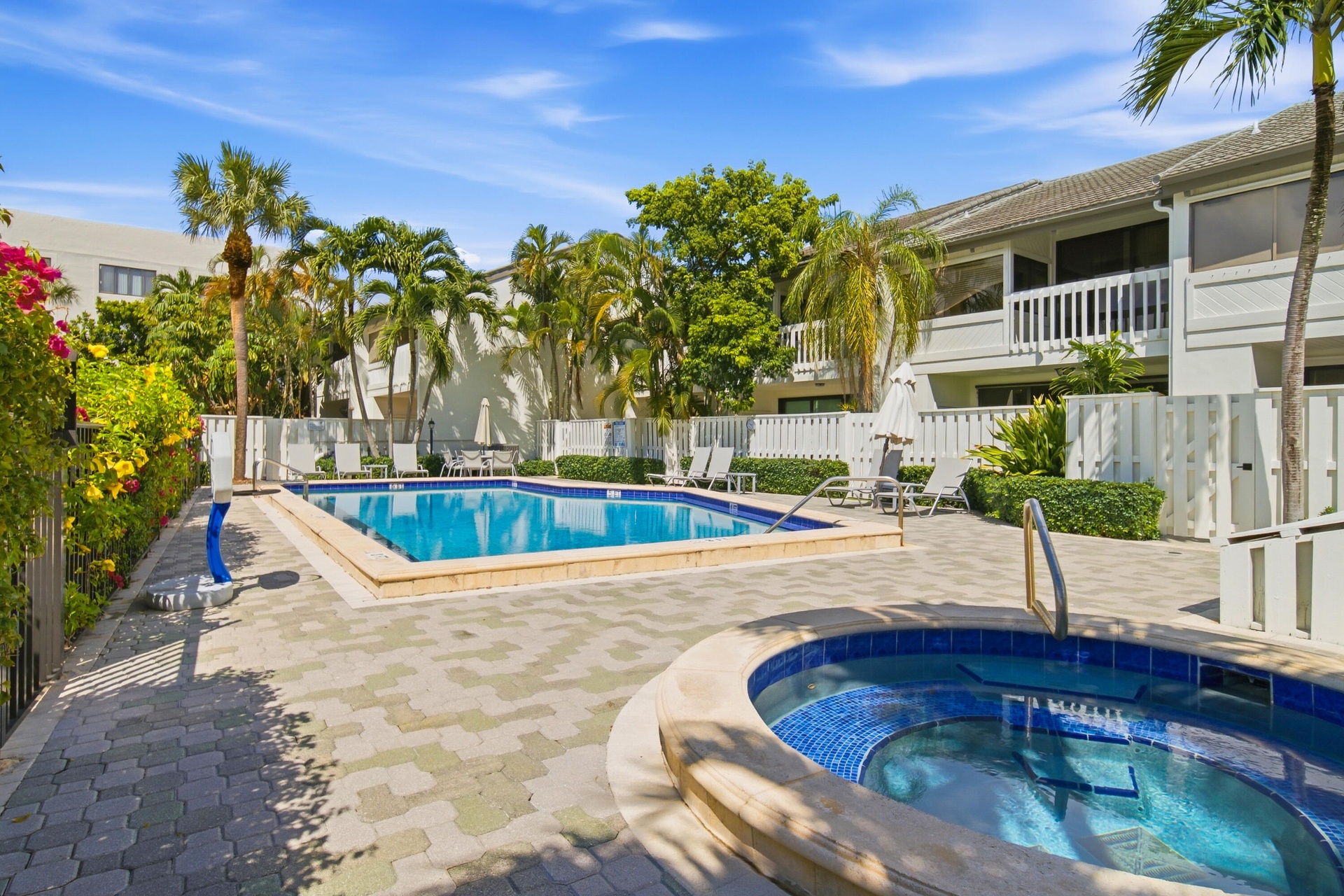 Resort-style pool with integrated spa, surrounded by paver patio, lush landscaping, and privacy fencing