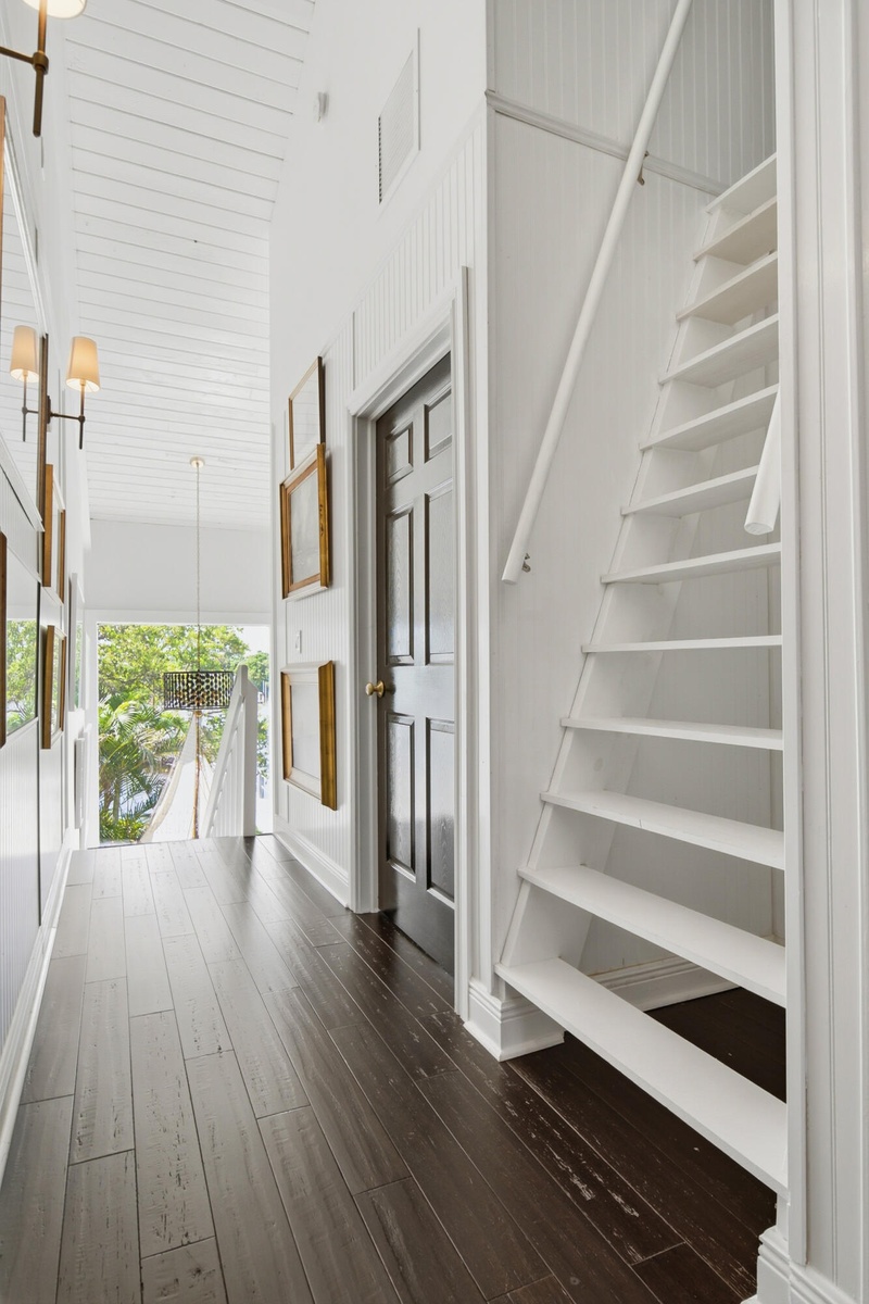 Dark wood-finish flooring, white paneled walls, exposed beam ceiling, built-in shelving, white staircase
