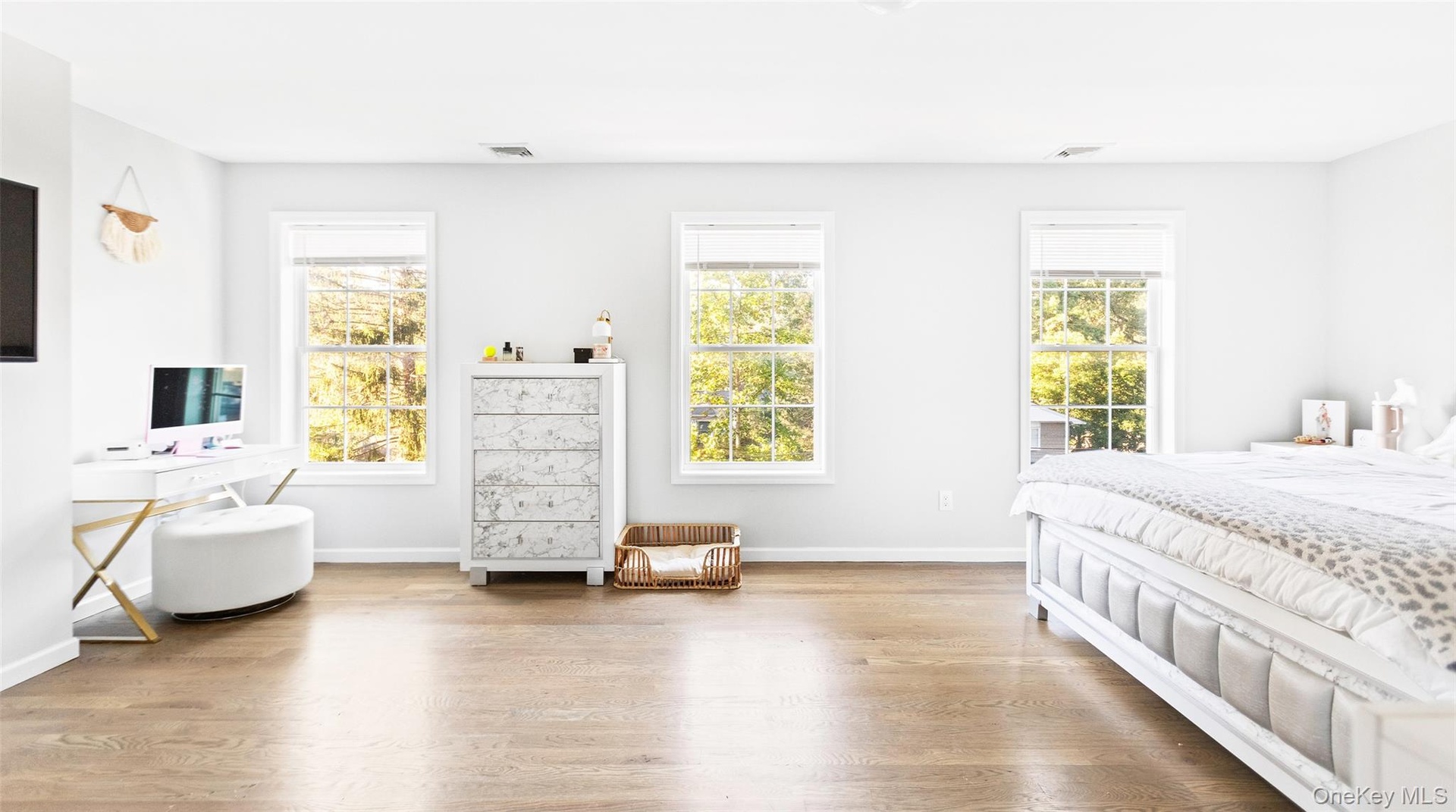 Light wood-finish flooring, three windows with white frames, white walls, and an upholstered bed frame