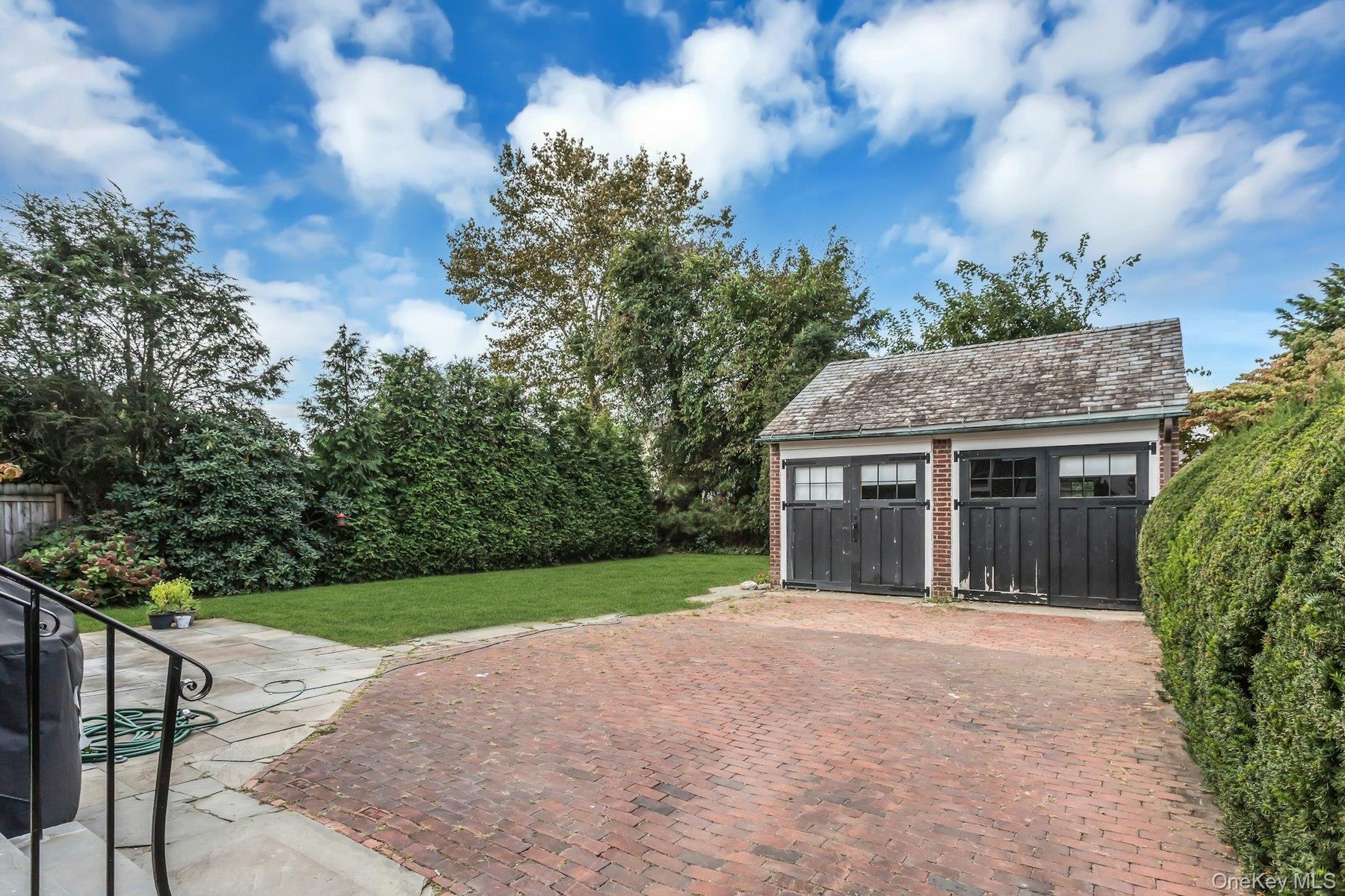Two-car detached garage with overhead doors, brick-paved driveway, and a manicured lawn area