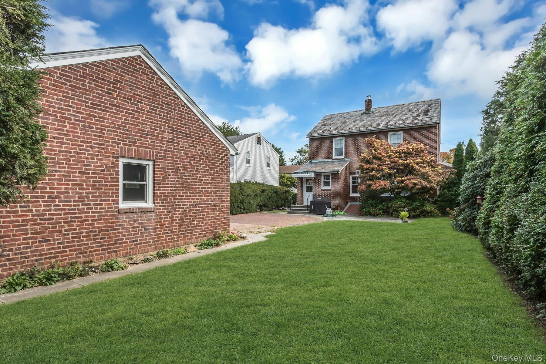 Expansive lawn, brick exterior, paved patio, and mature perimeter landscaping