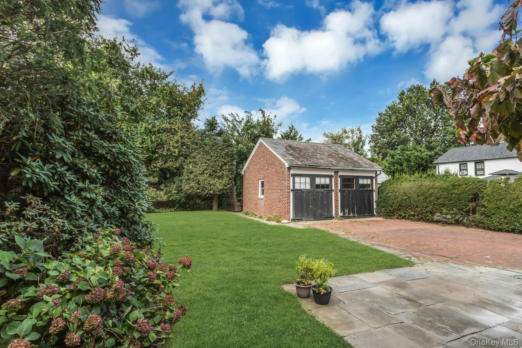 Brick garage with two carriage-style doors, a natural stone patio, and a brick paver driveway