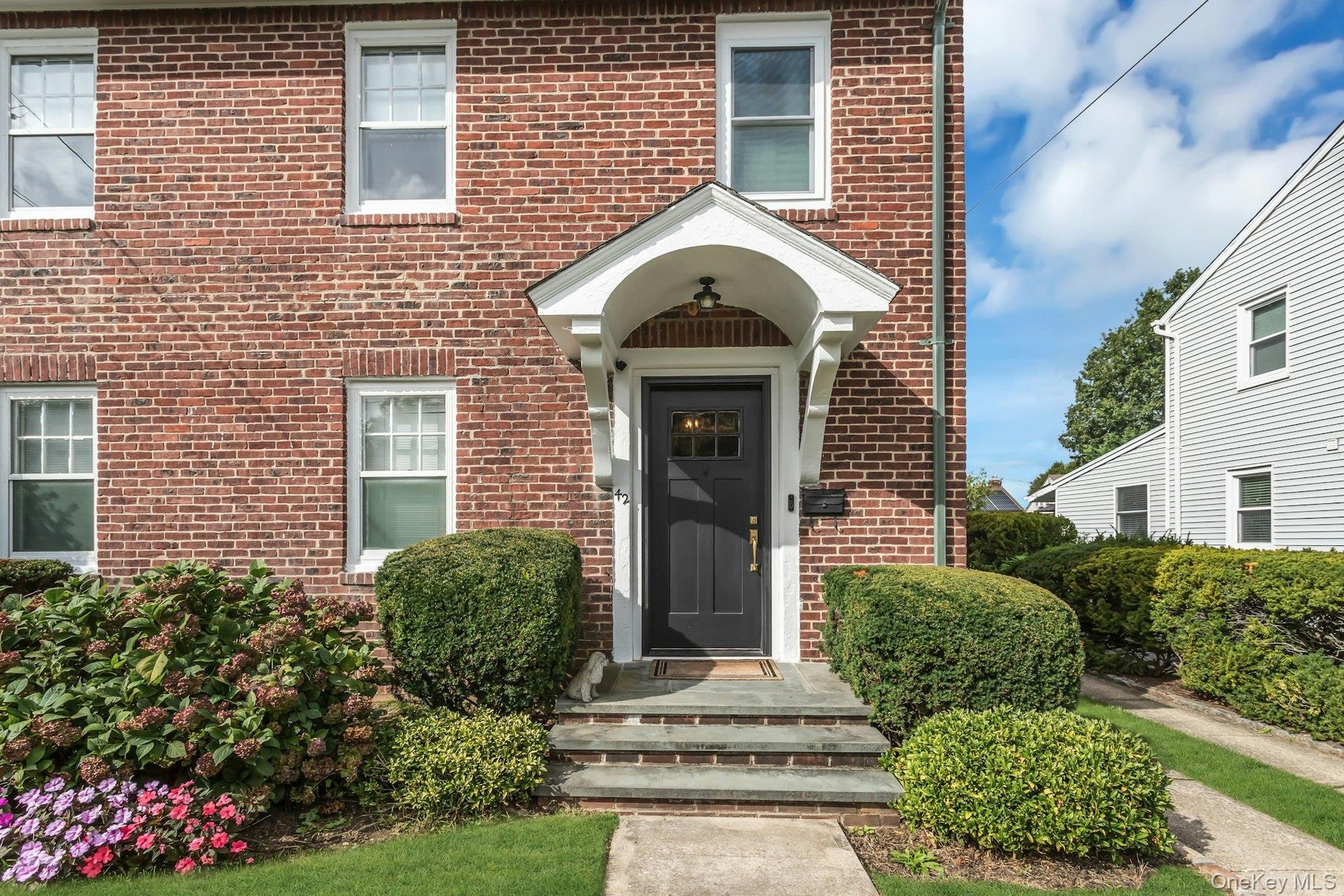 Red brick exterior with white trim windows and a dark panel front door, brick walkway and bluestone steps