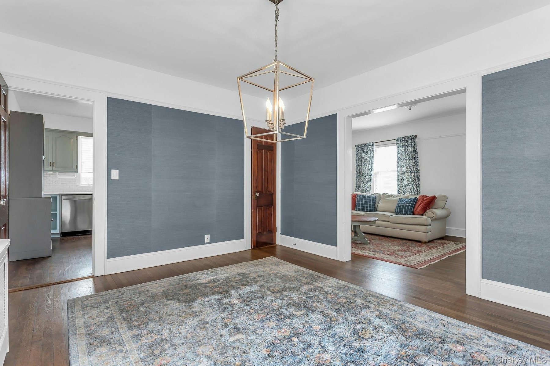 Hardwood flooring paired with a geometric metal chandelier, featuring an adjacent kitchen with stainless steel appliances and white subway tile backsp