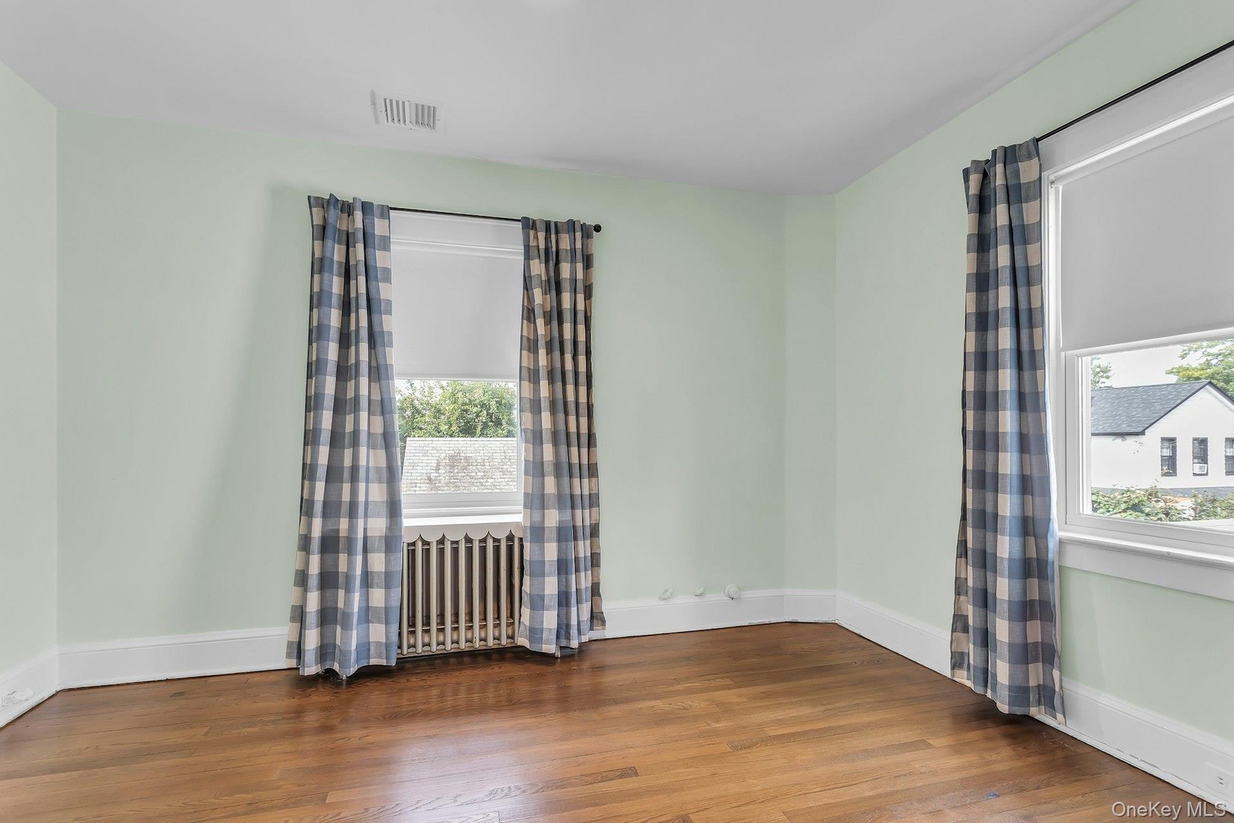 Hardwood flooring, two windows, radiator, and white trim