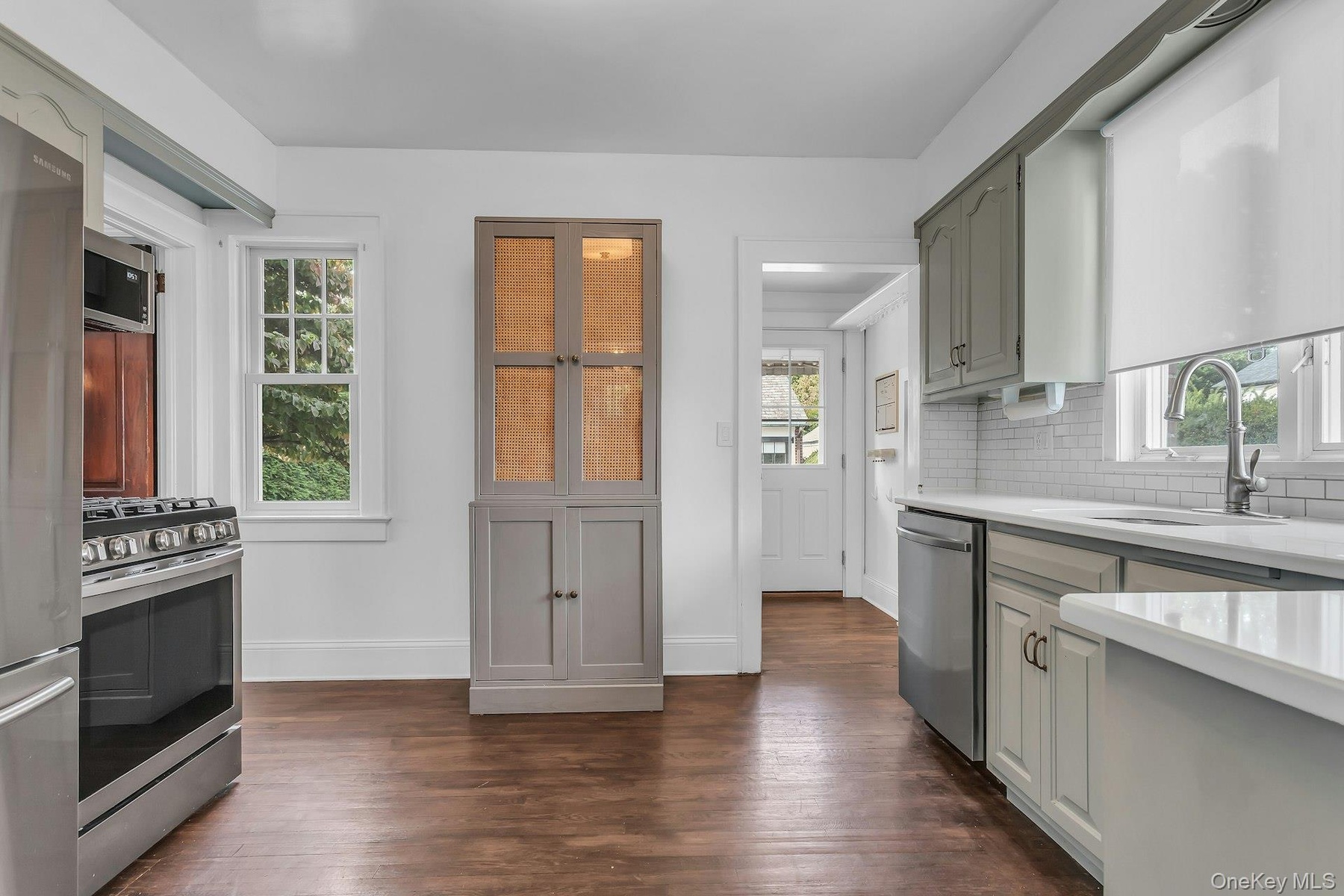 Stainless steel appliances, white subway tile backsplash, white countertops, built-in cabinetry, and wood-finish flooring