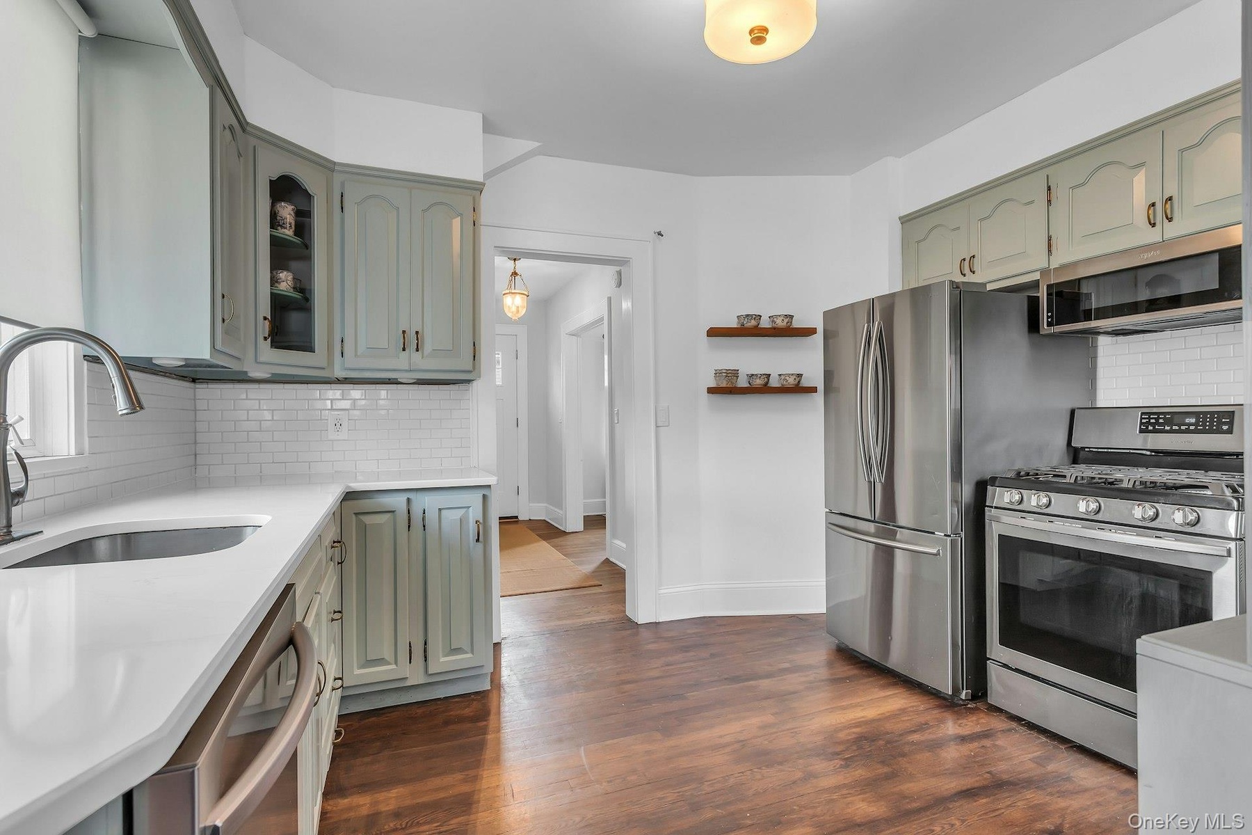 Kitchen featuring stainless steel appliances, wood-finish flooring, white countertops, subway tile backsplash, and light-toned cabinetry