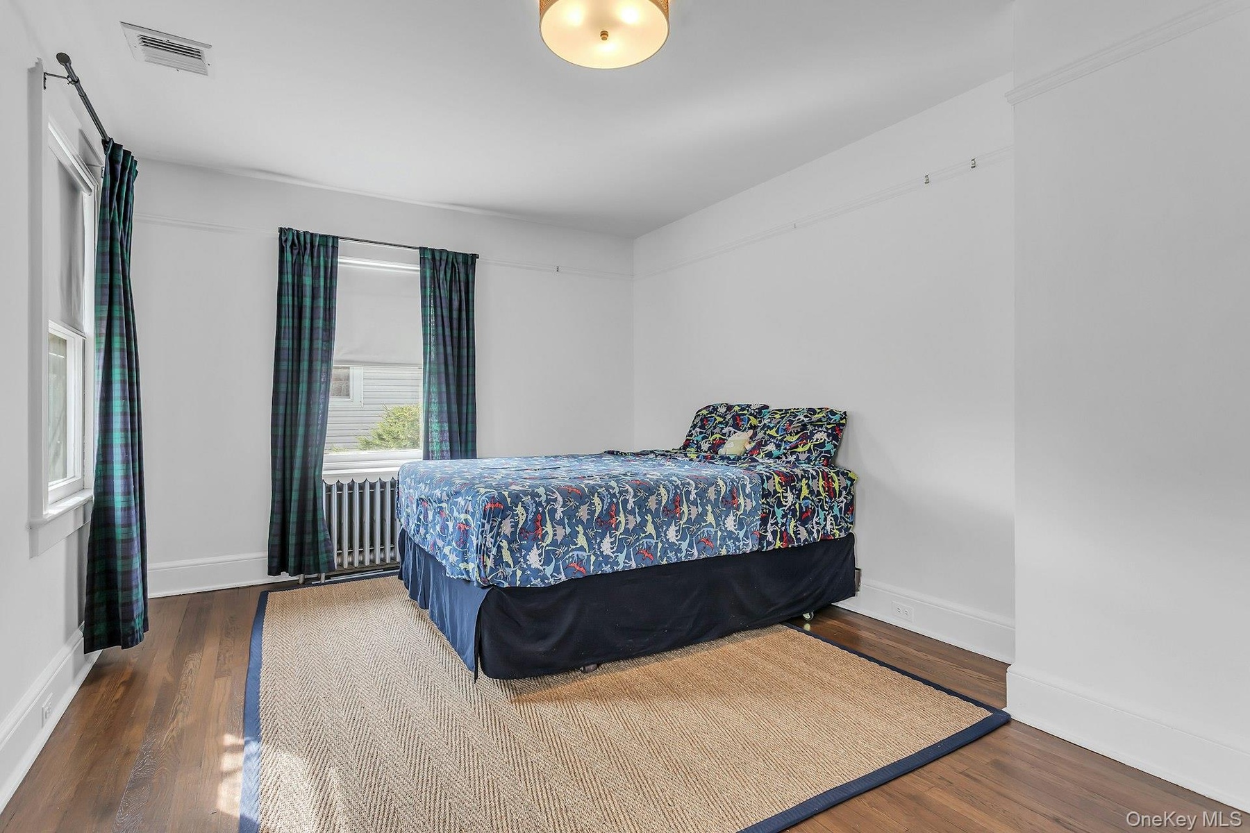 Hardwood flooring, painted walls, ceiling light fixture, and window with radiator below